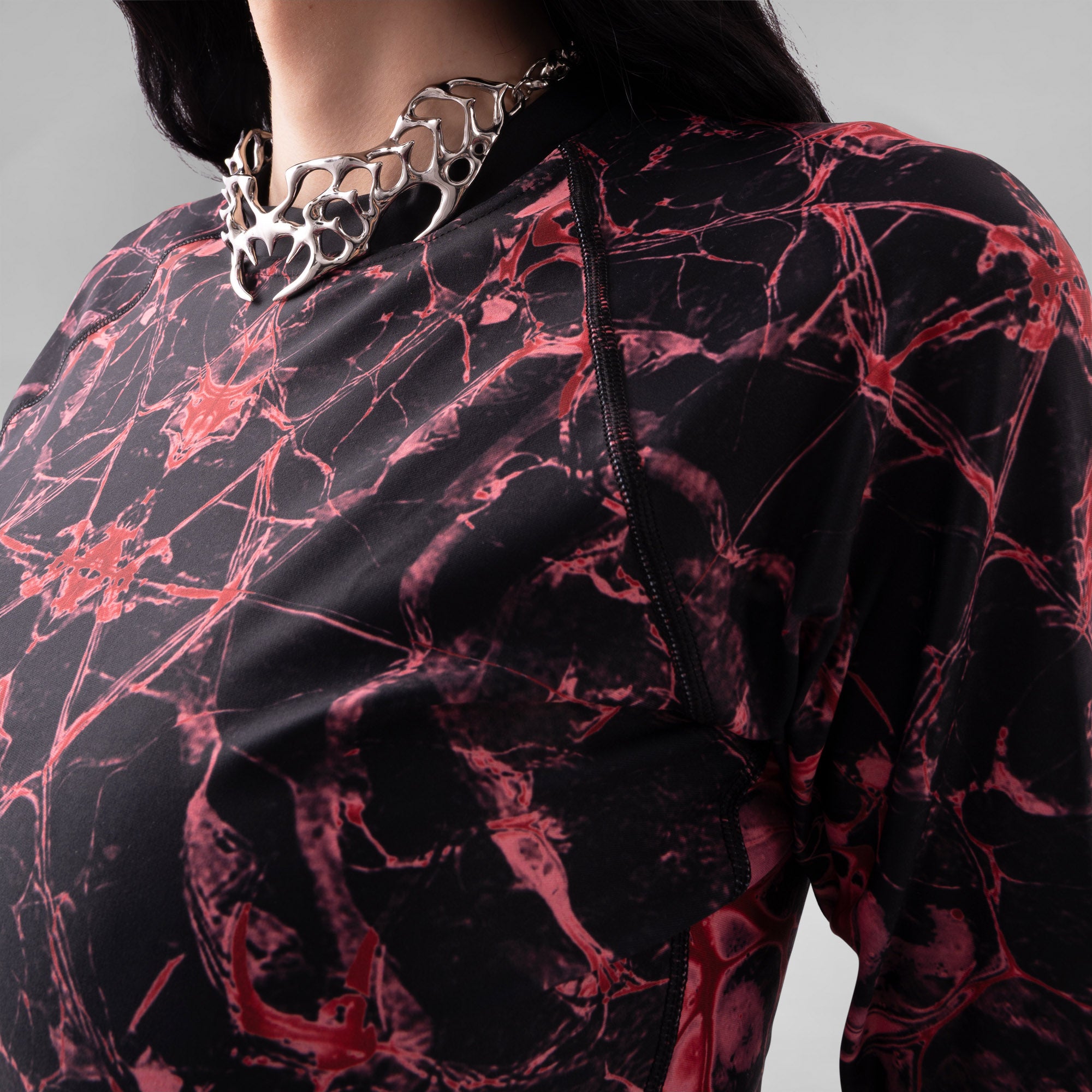 Person wearing a black and red marbled outfit with a silver necklace on a gray background