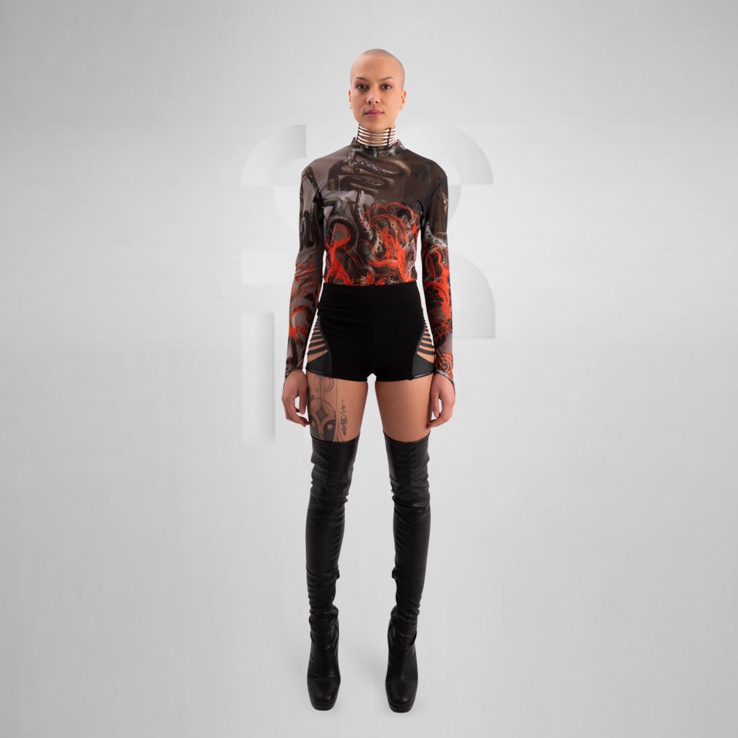 The image showcases a striking outfit featuring a long-sleeve top with an eye-catching design of swirling octopuses in dark hues, accented with vibrant red. The top is complemented by unique metallic neck detailing that adds an edgy flair. Paired with black high-waisted shorts featuring cut-out details, this look exudes confidence and individuality. Ideal for making a statement on the dancefloor or at a fashion-forward event, the ensemble beautifully blends art and style for a captivating appearance.