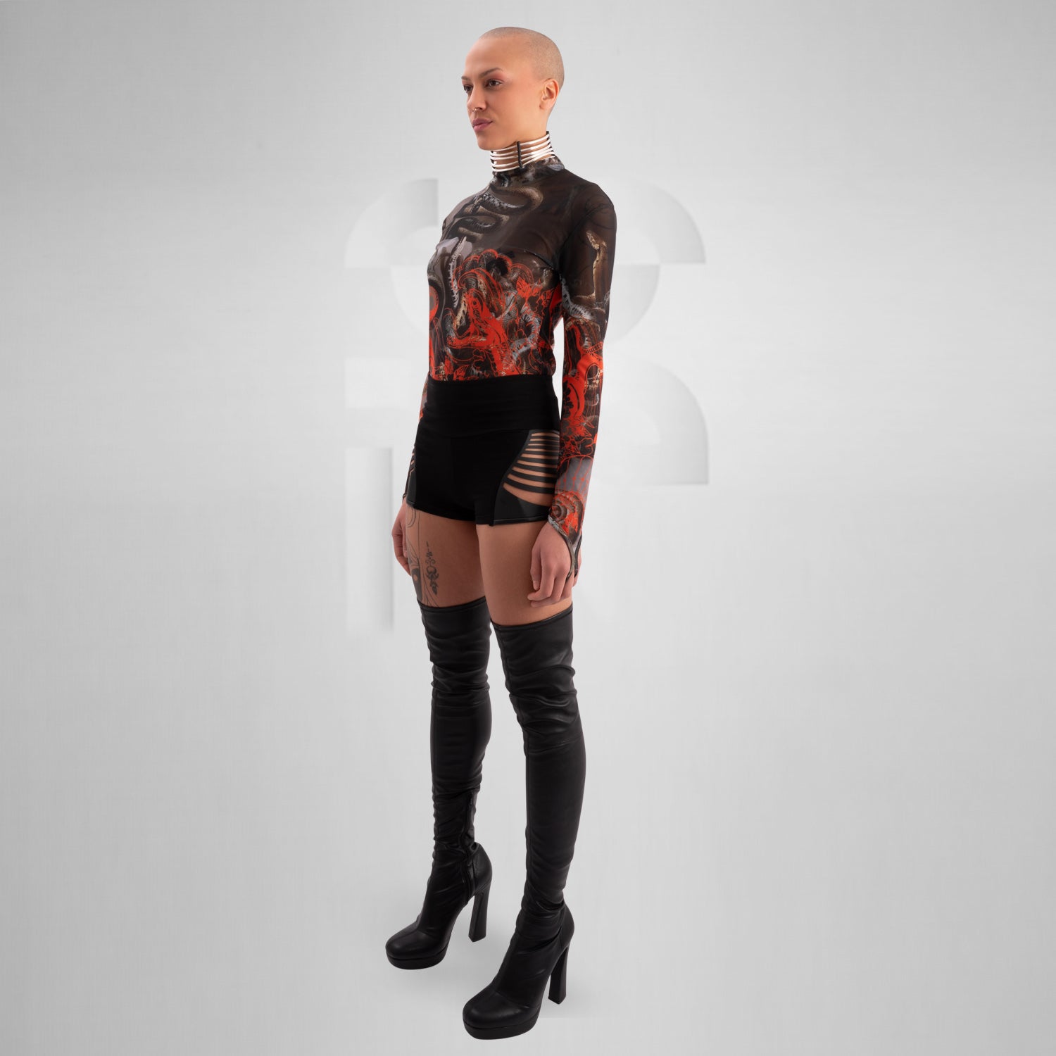 The image showcases a striking outfit featuring a long-sleeve top with an eye-catching design of swirling octopuses in dark hues, accented with vibrant red. The top is complemented by unique metallic neck detailing that adds an edgy flair. Paired with black high-waisted shorts featuring cut-out details, this look exudes confidence and individuality. Ideal for making a statement on the dancefloor or at a fashion-forward event, the ensemble beautifully blends art and style for a captivating appearance.