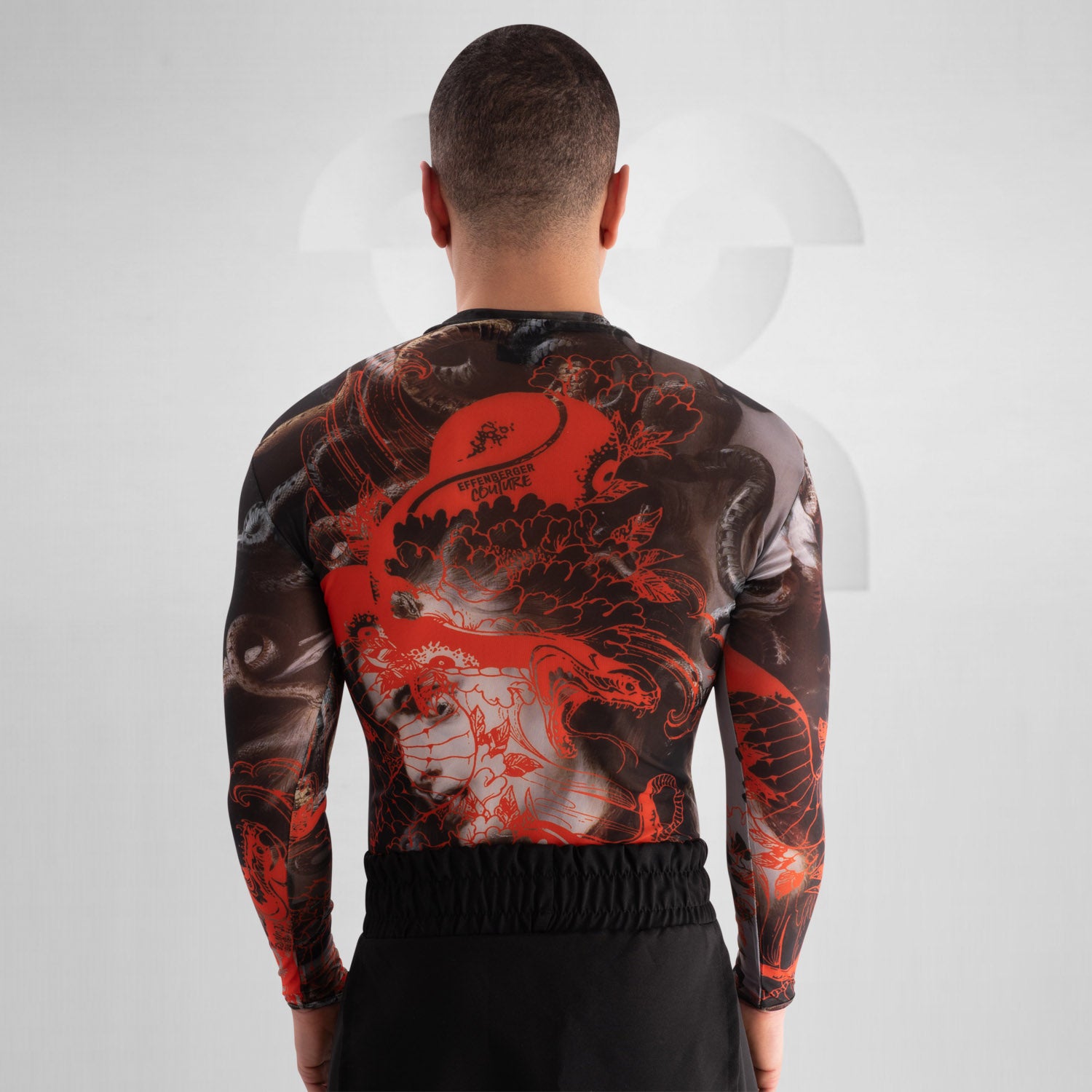 The image showcases a striking outfit featuring a long-sleeve top with an eye-catching design of swirling octopuses in dark hues, accented with vibrant red. The top is complemented by unique metallic neck detailing that adds an edgy flair. Paired with black high-waisted shorts featuring cut-out details, this look exudes confidence and individuality. Ideal for making a statement on the dancefloor or at a fashion-forward event, the ensemble beautifully blends art and style for a captivating appearance.