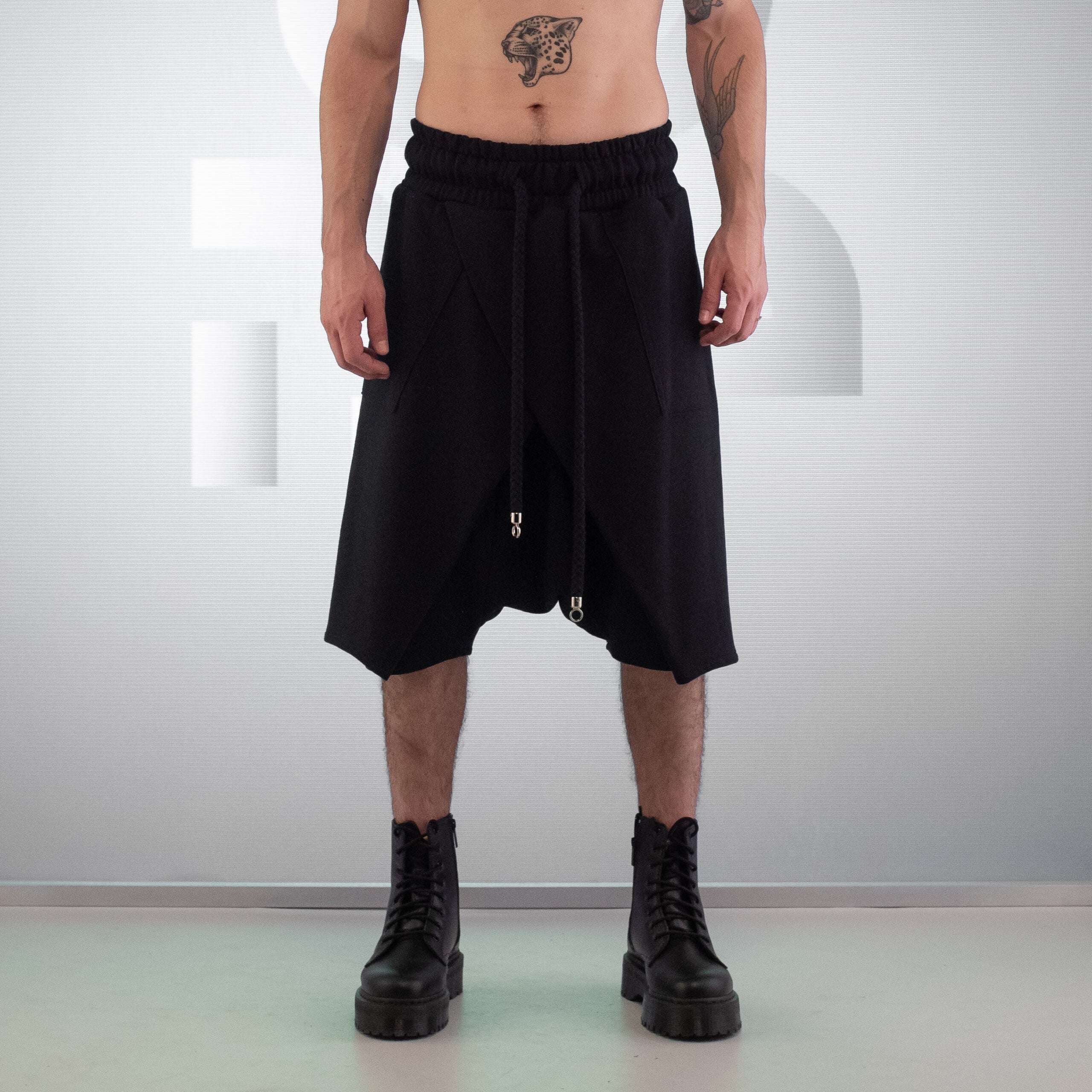 The image features the Asymmetric Shorts Mixed from This is Fred, showcasing a striking black design that combines comfort and avant-garde style. With a relaxed fit and an elastic waistband, these shorts offer unrestricted movement, making them perfect for urban adventures or club nights. The unique asymmetric cut and drawstring details add an edgy flair, while the versatile design allows you to pair them with a variety of looks. Ideal for making a bold fashion statement!
