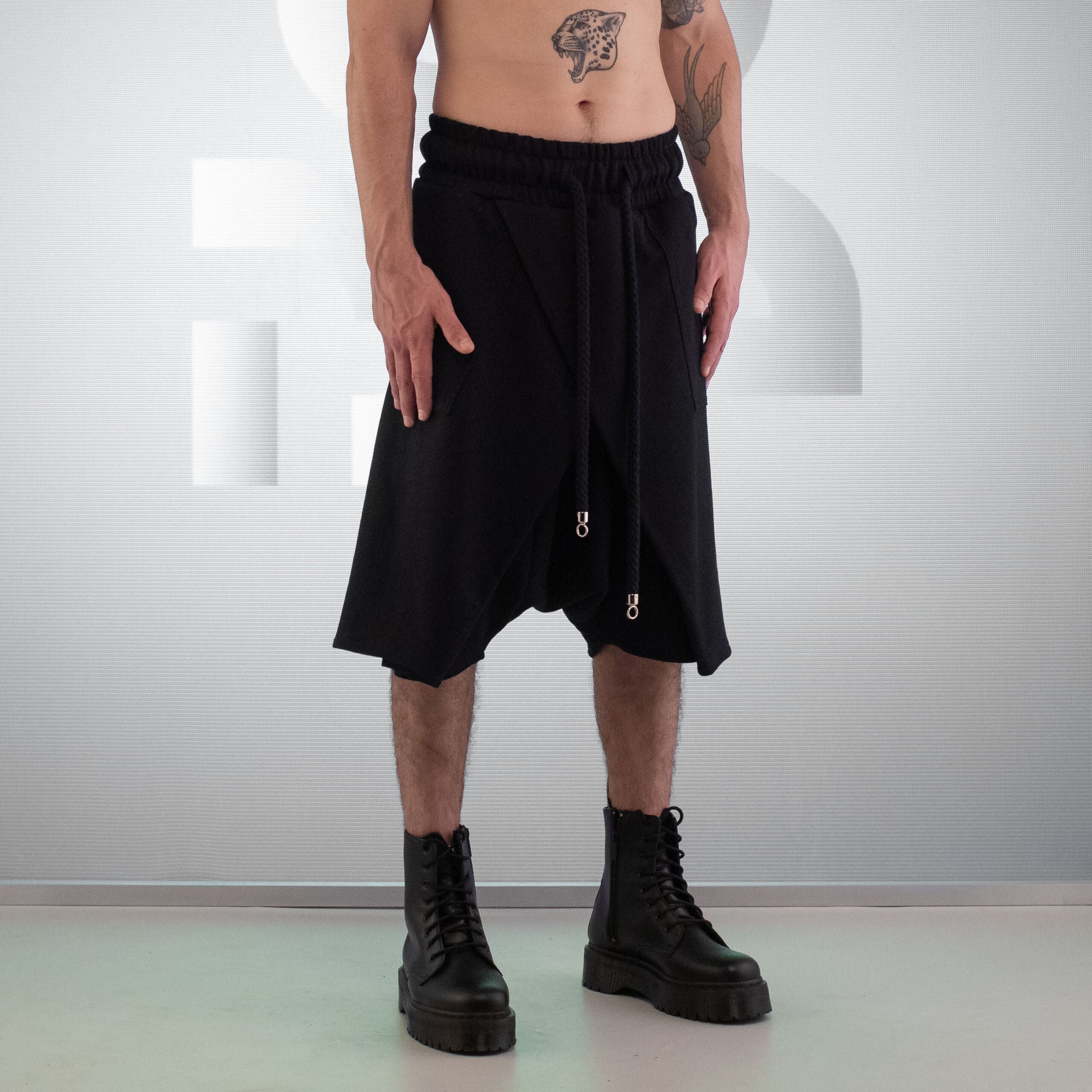 The image features the Asymmetric Shorts Mixed from This is Fred, showcasing a striking black design that combines comfort and avant-garde style. With a relaxed fit and an elastic waistband, these shorts offer unrestricted movement, making them perfect for urban adventures or club nights. The unique asymmetric cut and drawstring details add an edgy flair, while the versatile design allows you to pair them with a variety of looks. Ideal for making a bold fashion statement!