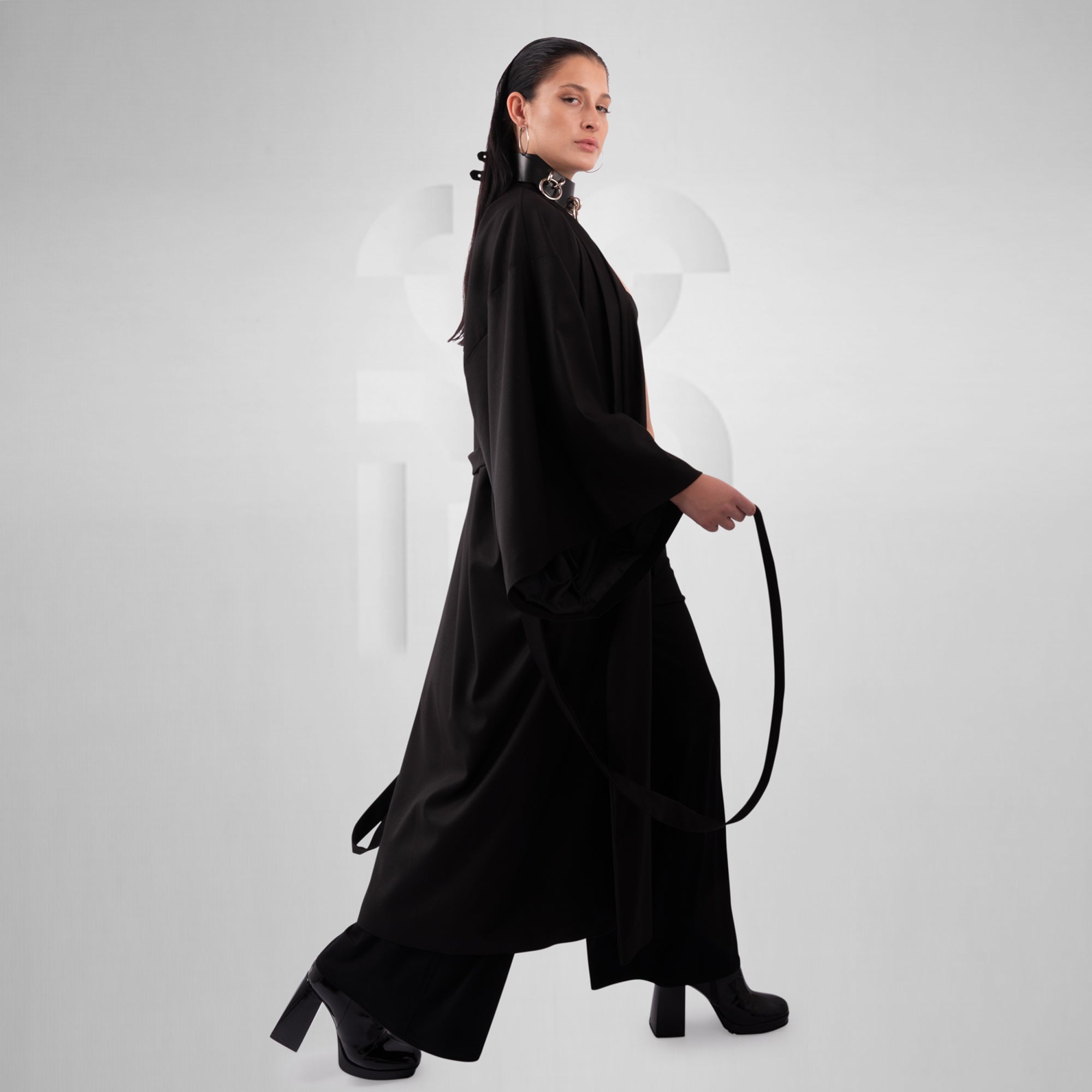 Woman wearing a long black dress holding a whip on a white background