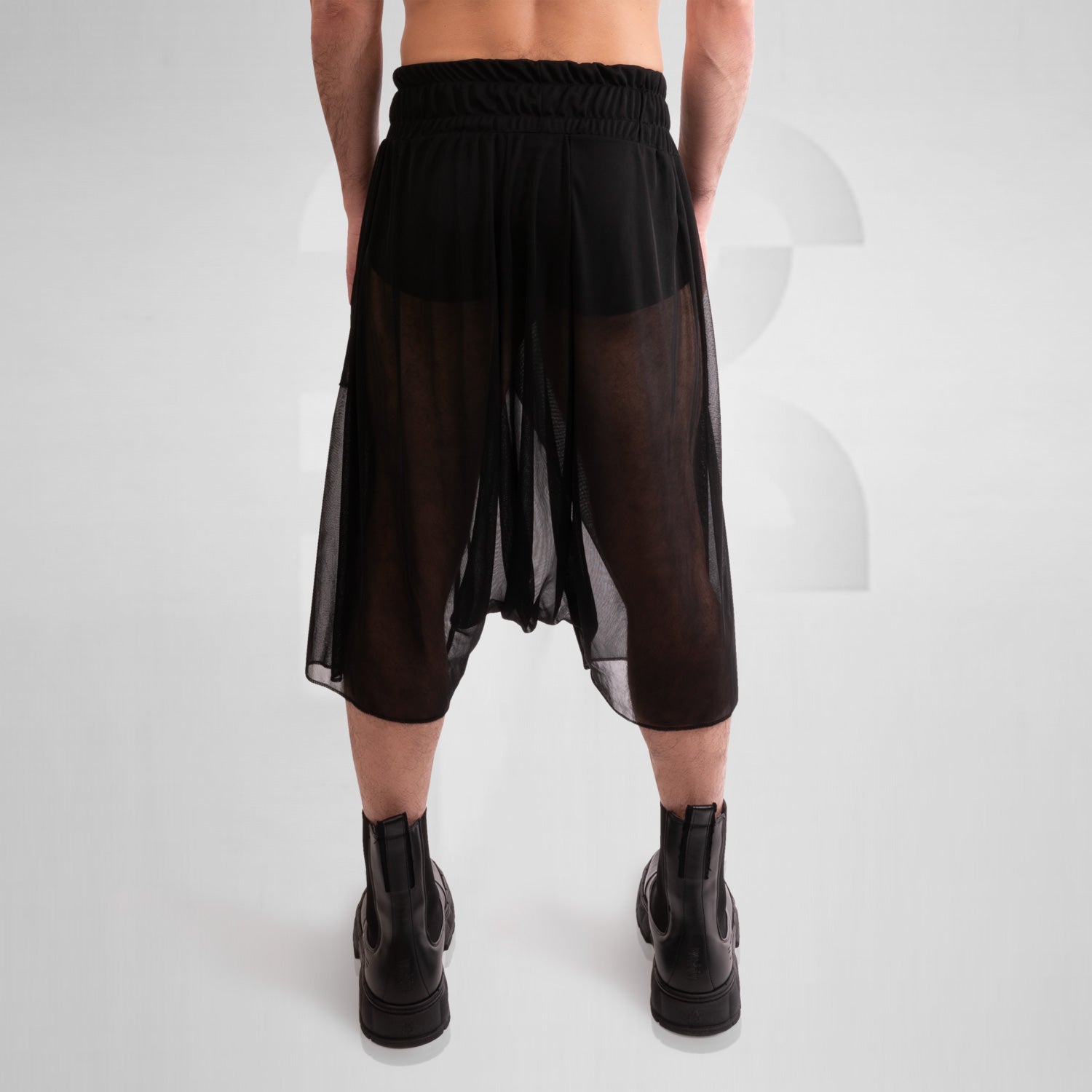 Avantgarde Mesh Shorts from This is Fred, showcasing a bold silhouette and breathable mesh design, perfect for high-fashion looks and vibrant techno parties. Styled with sleek black boots.