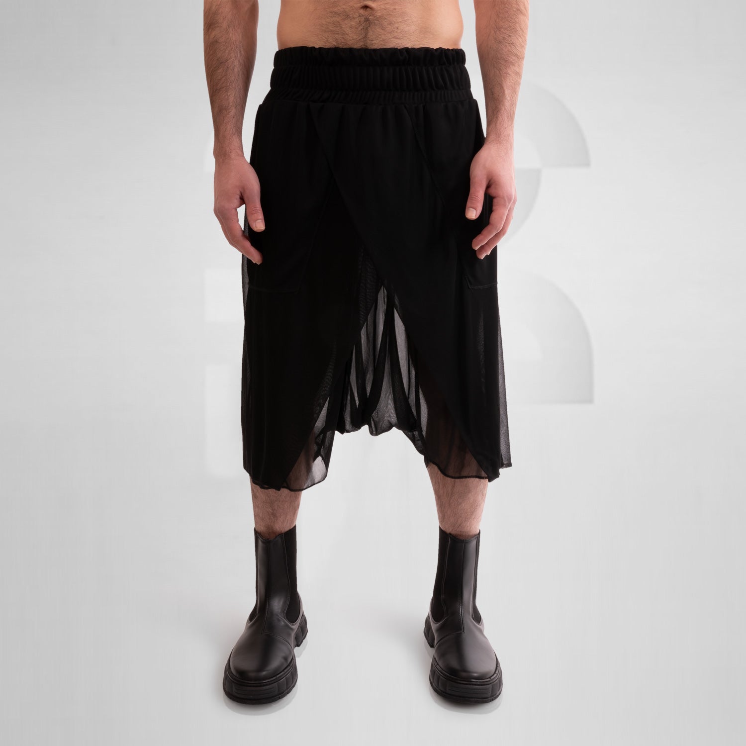 Avantgarde Mesh Shorts from This is Fred, showcasing a bold silhouette and breathable mesh design, perfect for high-fashion looks and vibrant techno parties. Styled with sleek black boots.