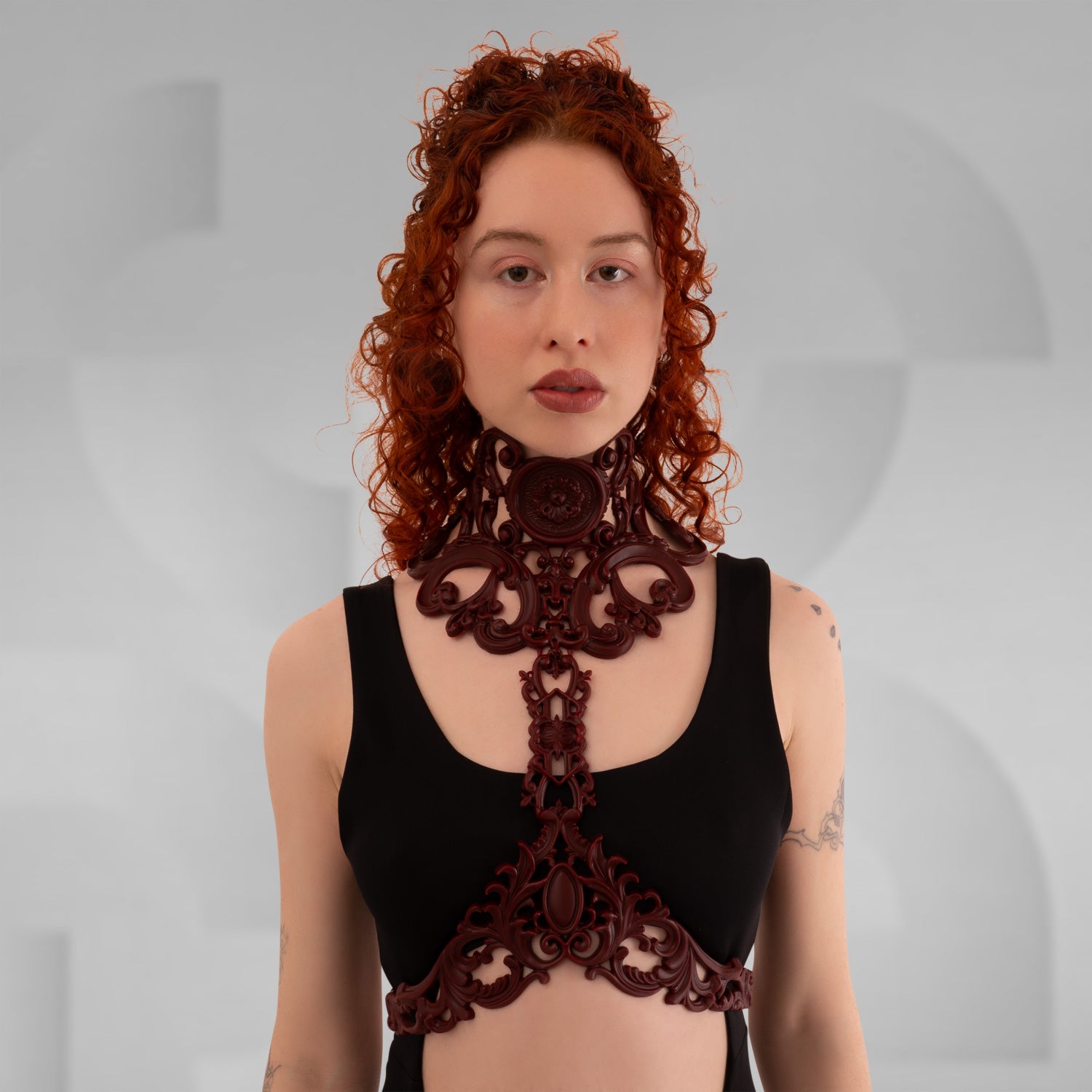 This image showcases a model wearing an elegant dark red harness that features intricate baroque detailing. The harness beautifully frames the model's neckline, combining artistic design with a modern flair. Its bold structure adds a striking element to the outfit, making it an excellent choice for those who embrace avant-garde fashion. Perfect for nightlife events or enhancing a casual look, this piece exudes confidence and sophistication.