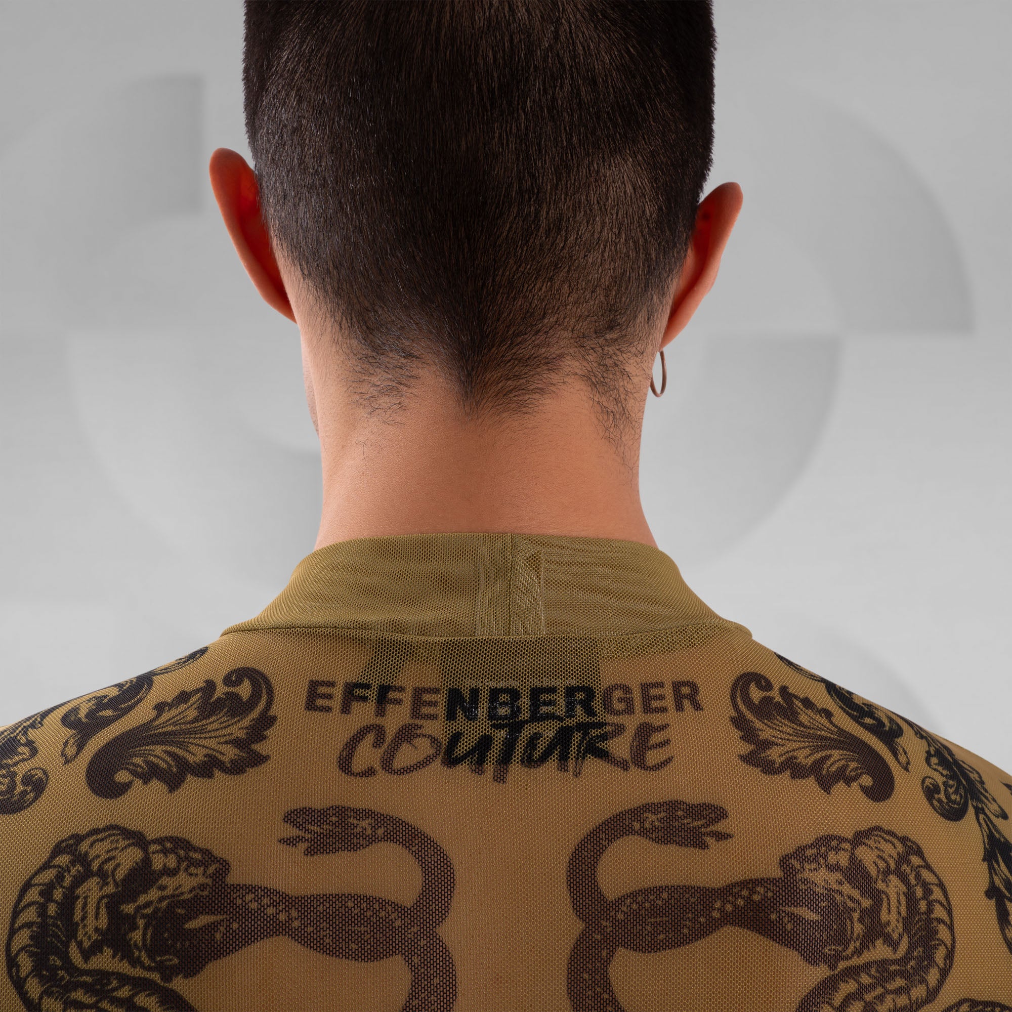 Person wearing a brown jacket with snake designs and 'Effenberger Couture' branding on a plain background