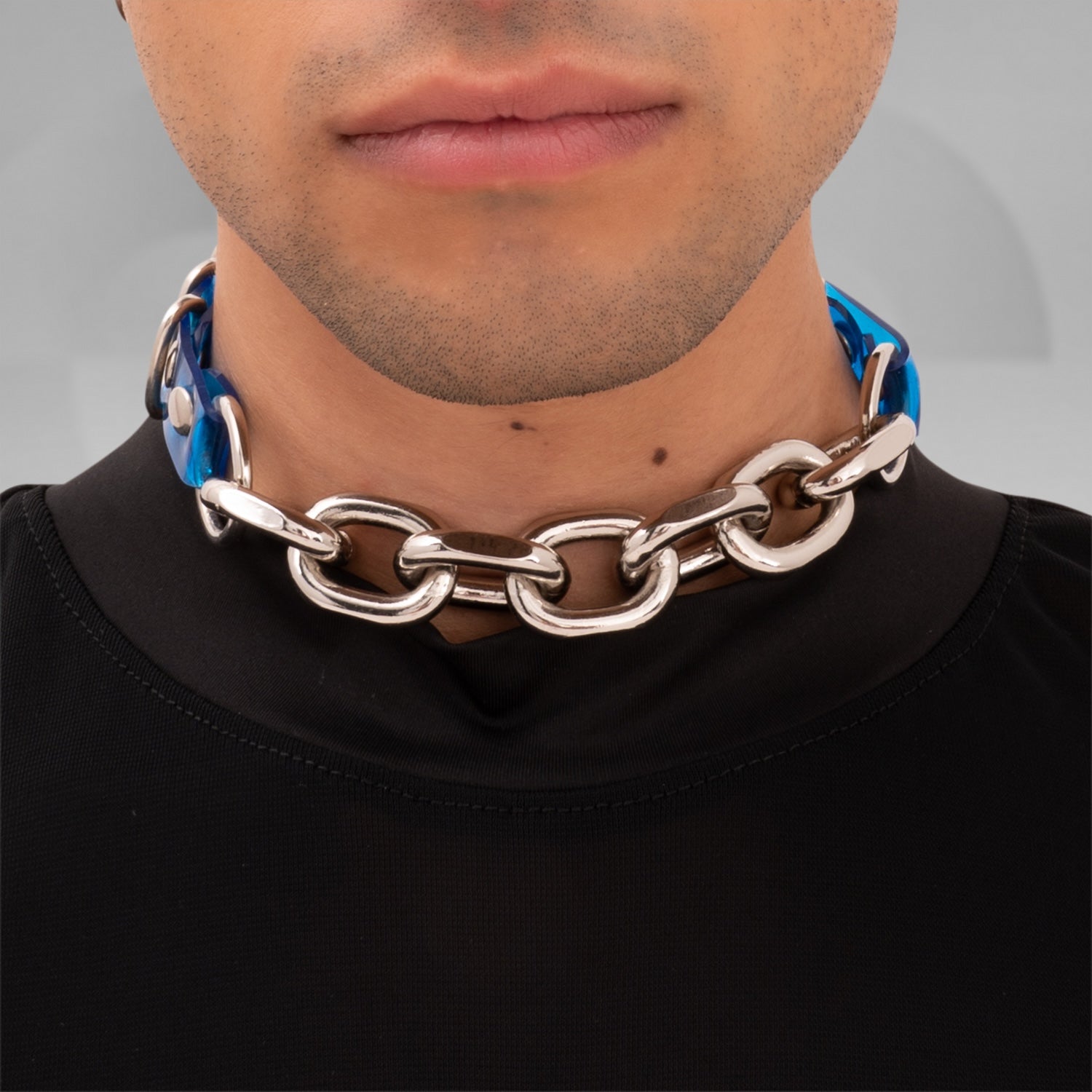 The image shows a person wearing a chunky chain choker with large metallic links. The choker sits snugly around the neck, adding a bold, edgy accent to the outfit. The chain appears to have a sturdy, polished finish, enhancing its statement-making quality. The individual is dressed in black, which complements the choker and highlights its striking design