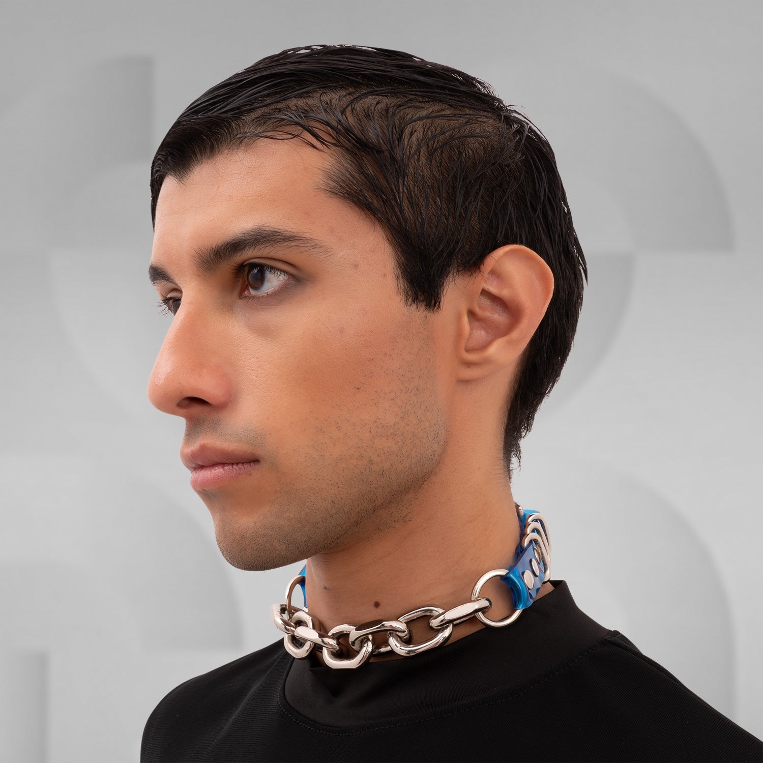 The image shows a person wearing a chunky chain choker with large metallic links. The choker sits snugly around the neck, adding a bold, edgy accent to the outfit. The chain appears to have a sturdy, polished finish, enhancing its statement-making quality. The individual is dressed in black, which complements the choker and highlights its striking design