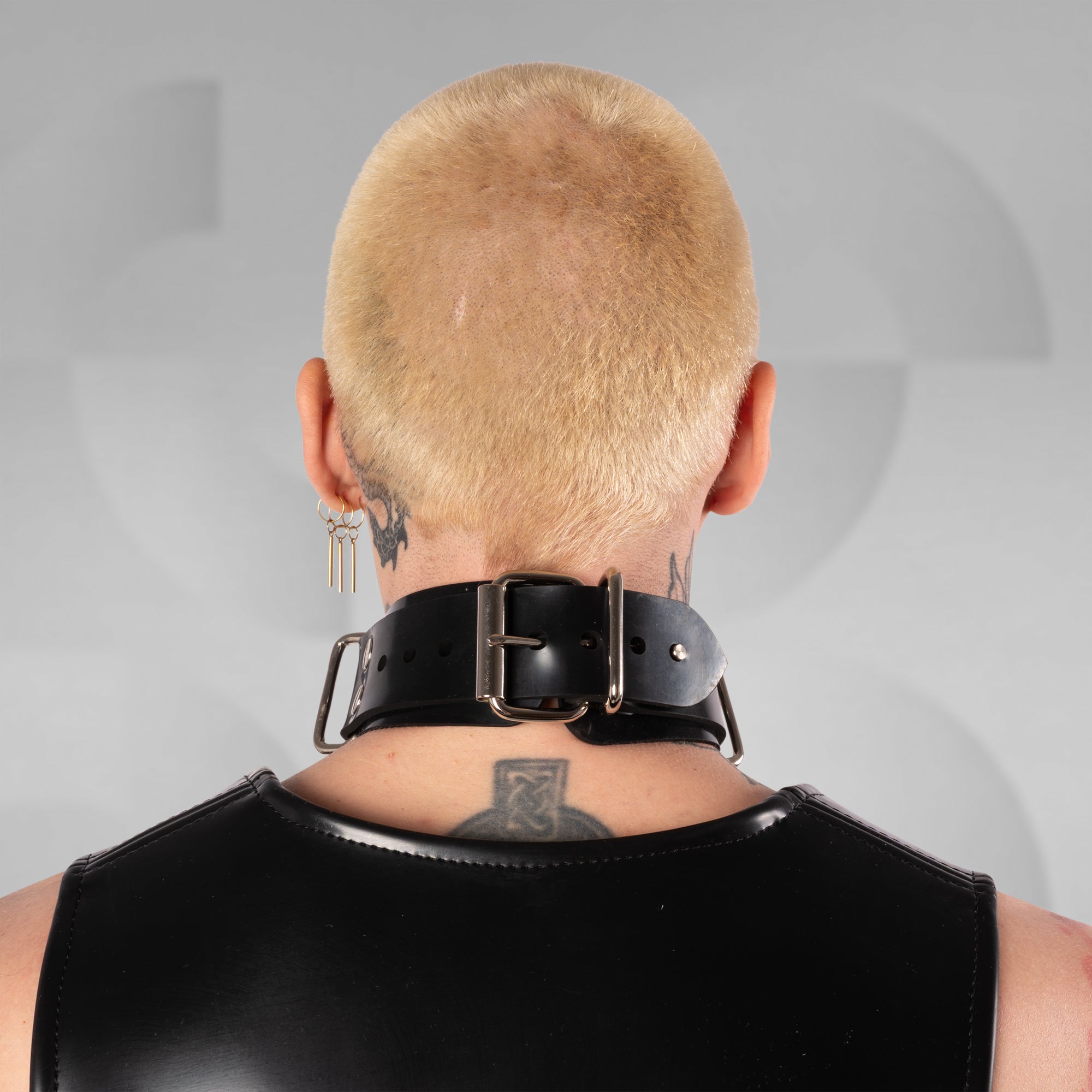 Person wearing a black leather choker and shoulder harness against a gray background