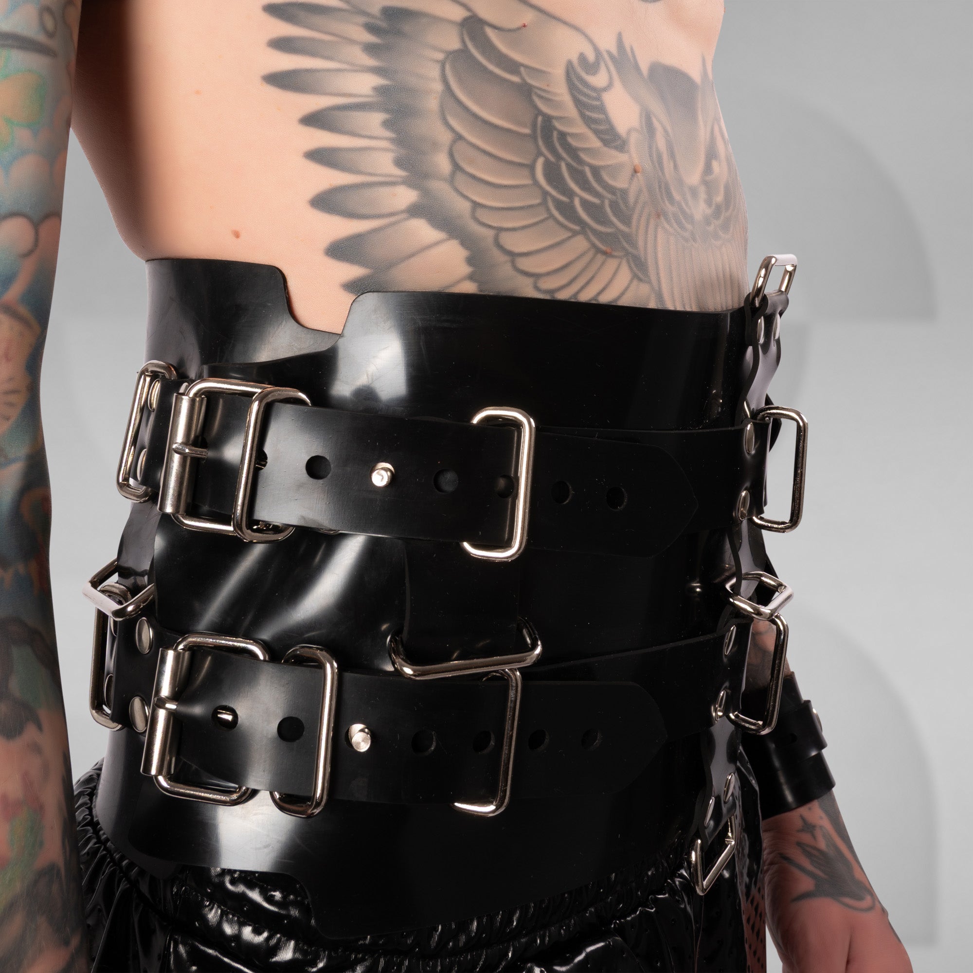 Person wearing a black leather harness with metal buckles on a gray background
