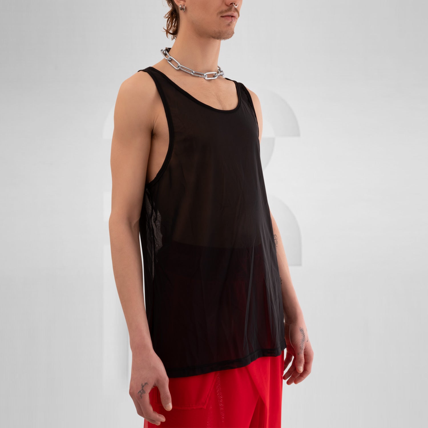 The image features a bold black mesh tank top, designed for the fashion-forward individual looking to make a statement. This sheer piece exudes an edgy vibe, perfect for layering over vibrant ensembles or wearing solo for a striking look. The relaxed fit offers comfort while the unique design highlights individuality, making it ideal for both clubwear and casual outings. Elevate your style and embrace your daring side with this standout top that effortlessly combines modern aesthetics and versatility!