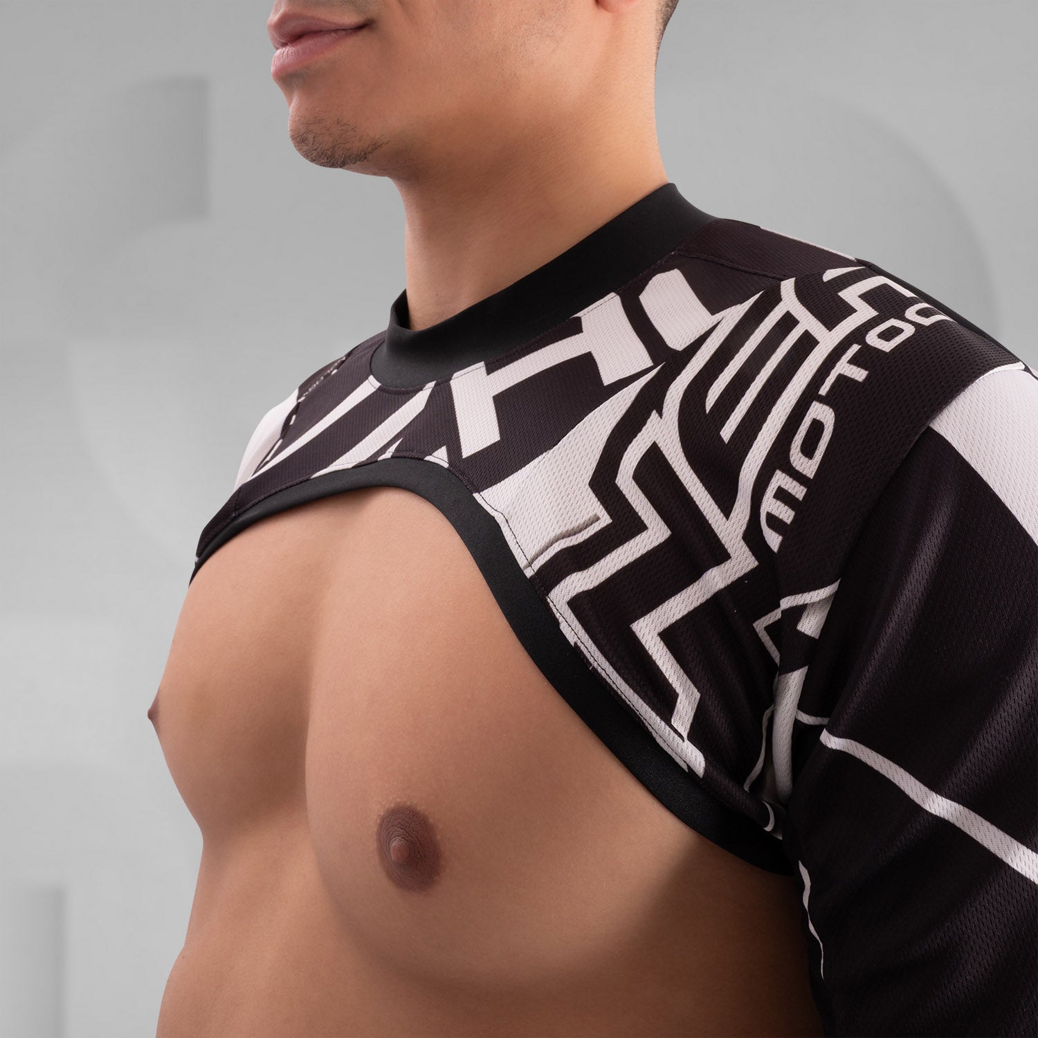 The image showcases a person wearing a bold, geometric outfit with strong black and white patterns. The top is a distinctive design featuring long sleeves and an open front, creating an avant-garde look. The matching pants continue the geometric theme. The overall style is modern and edgy, reflecting influences from both high fashion and the techno music scene.