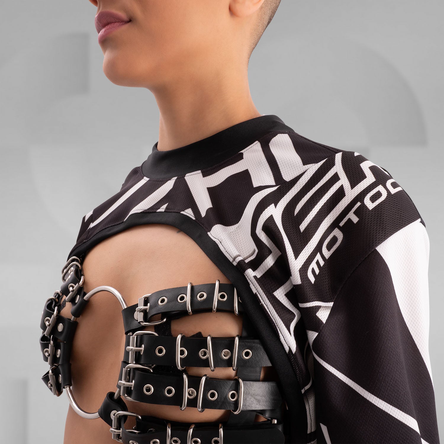 The image showcases a person wearing a bold, geometric outfit with strong black and white patterns. The top is a distinctive design featuring long sleeves and an open front, creating an avant-garde look. The matching pants continue the geometric theme. The overall style is modern and edgy, reflecting influences from both high fashion and the techno music scene.