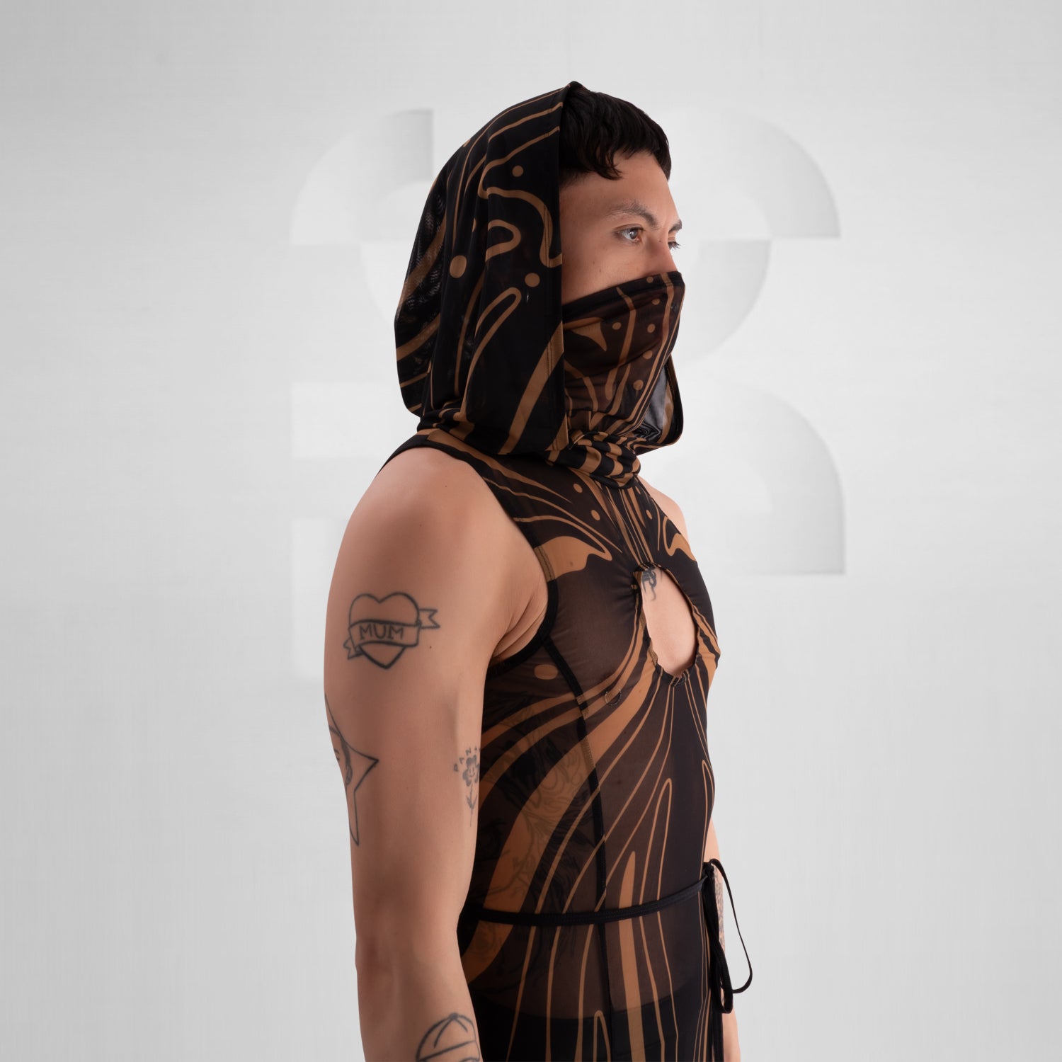 The image showcases a striking, futuristic sheer dress with intricate gold detailing and a matching hood, creating a bold and avant-garde look.