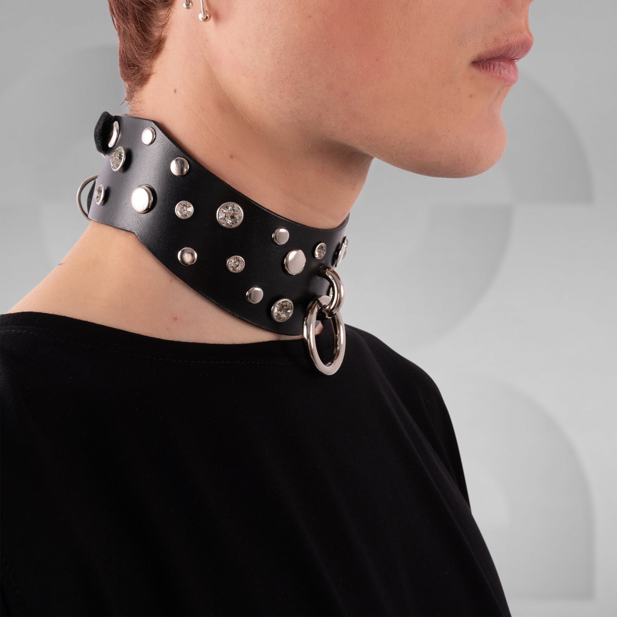 Black leather choker with studs and rings worn by a person on a gray background