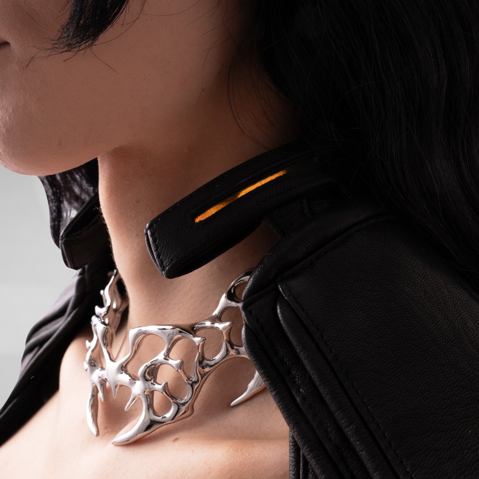Close-up of a person wearing a black leather outfit with a metallic necklace.