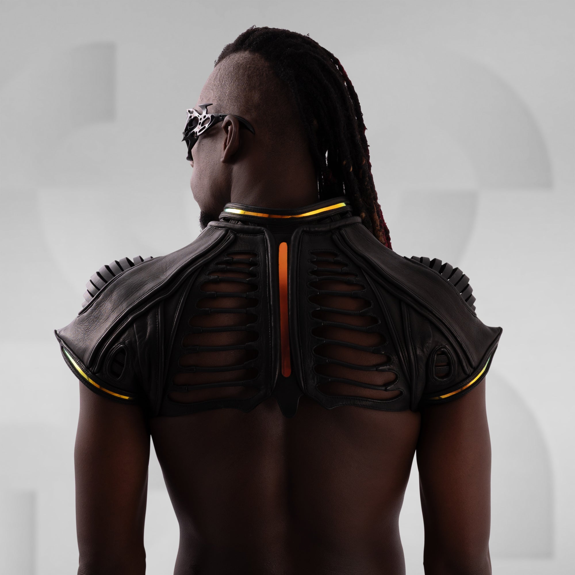 Person wearing a black leather shoulder piece with orange accents on a plain background