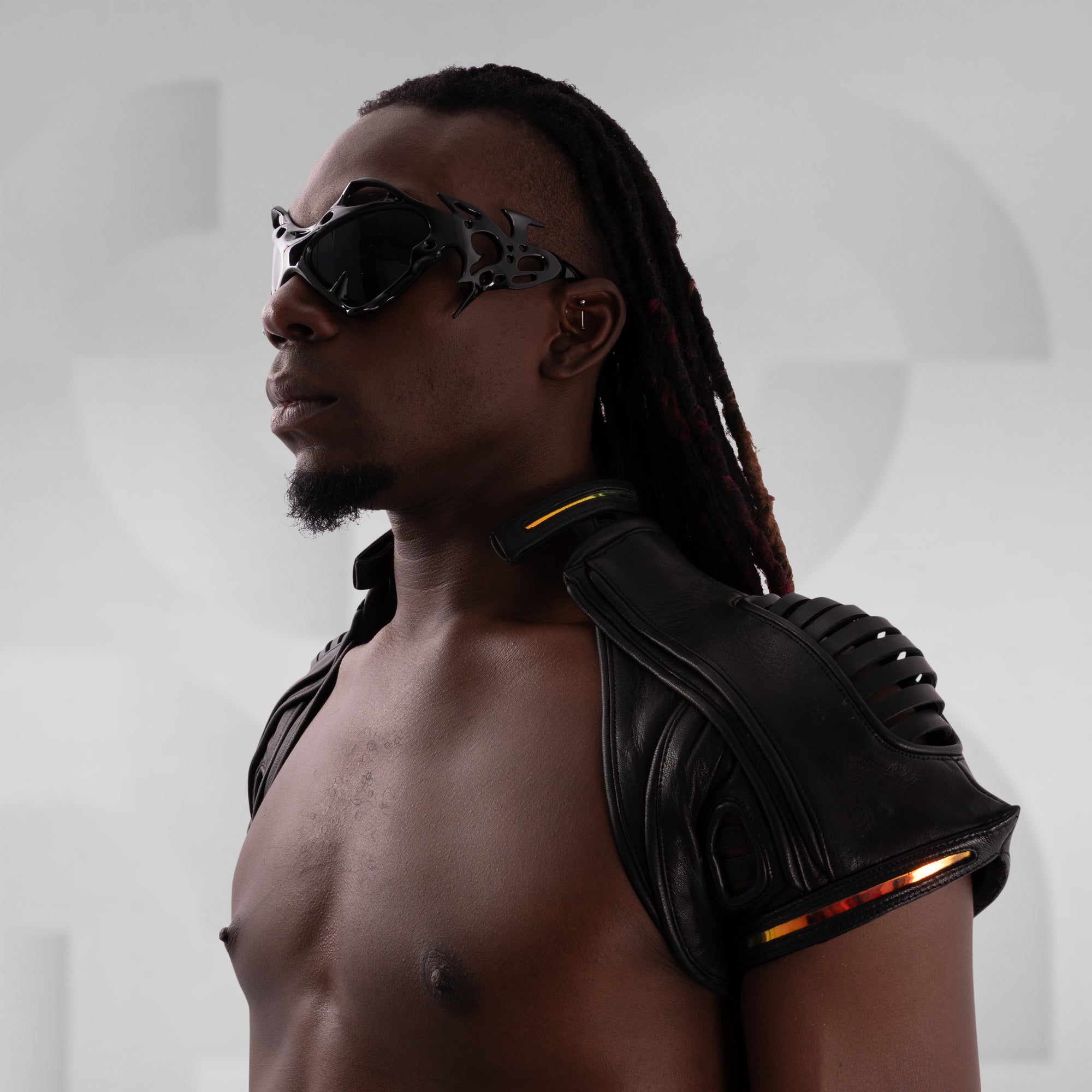 Man wearing futuristic goggles and leather shoulder pads against a white background