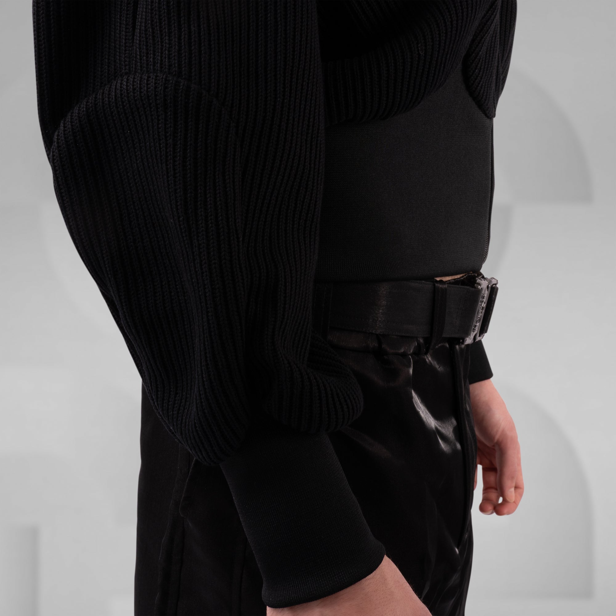 Person wearing a black ribbed sweater and black pants on a light gray background