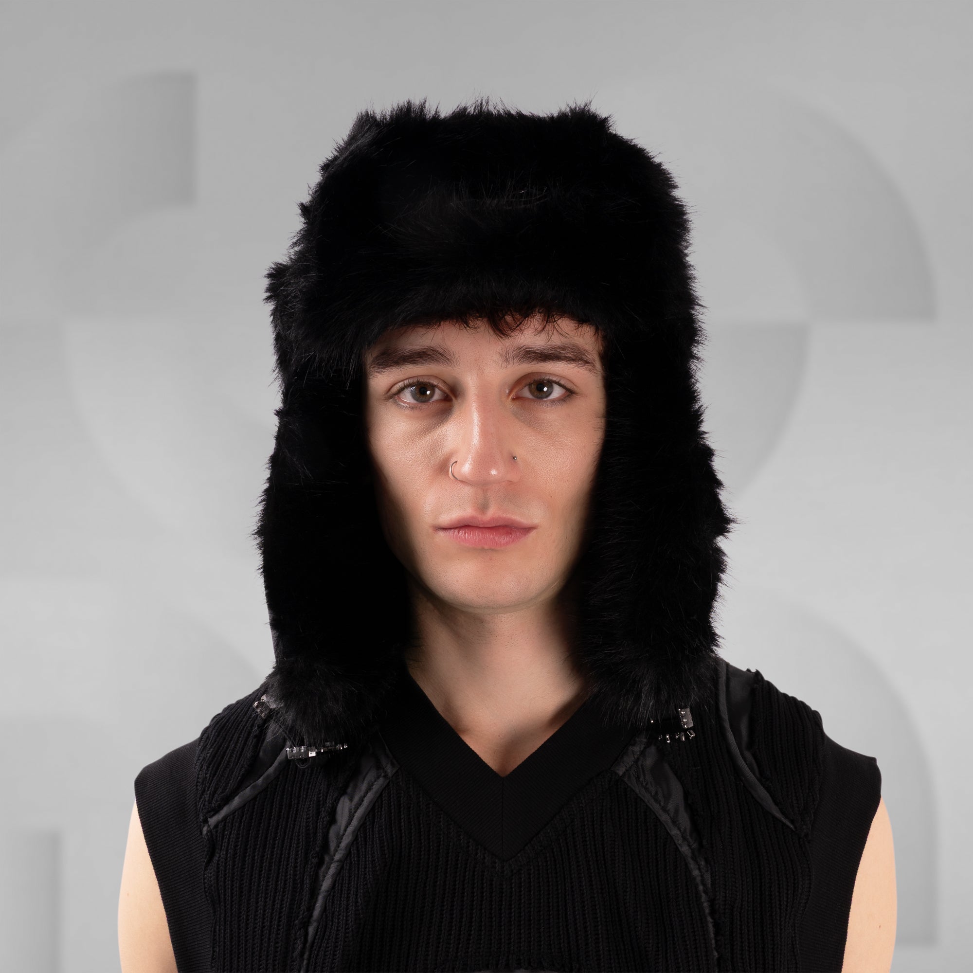 Person wearing a black fur-trimmed hat against a gray background