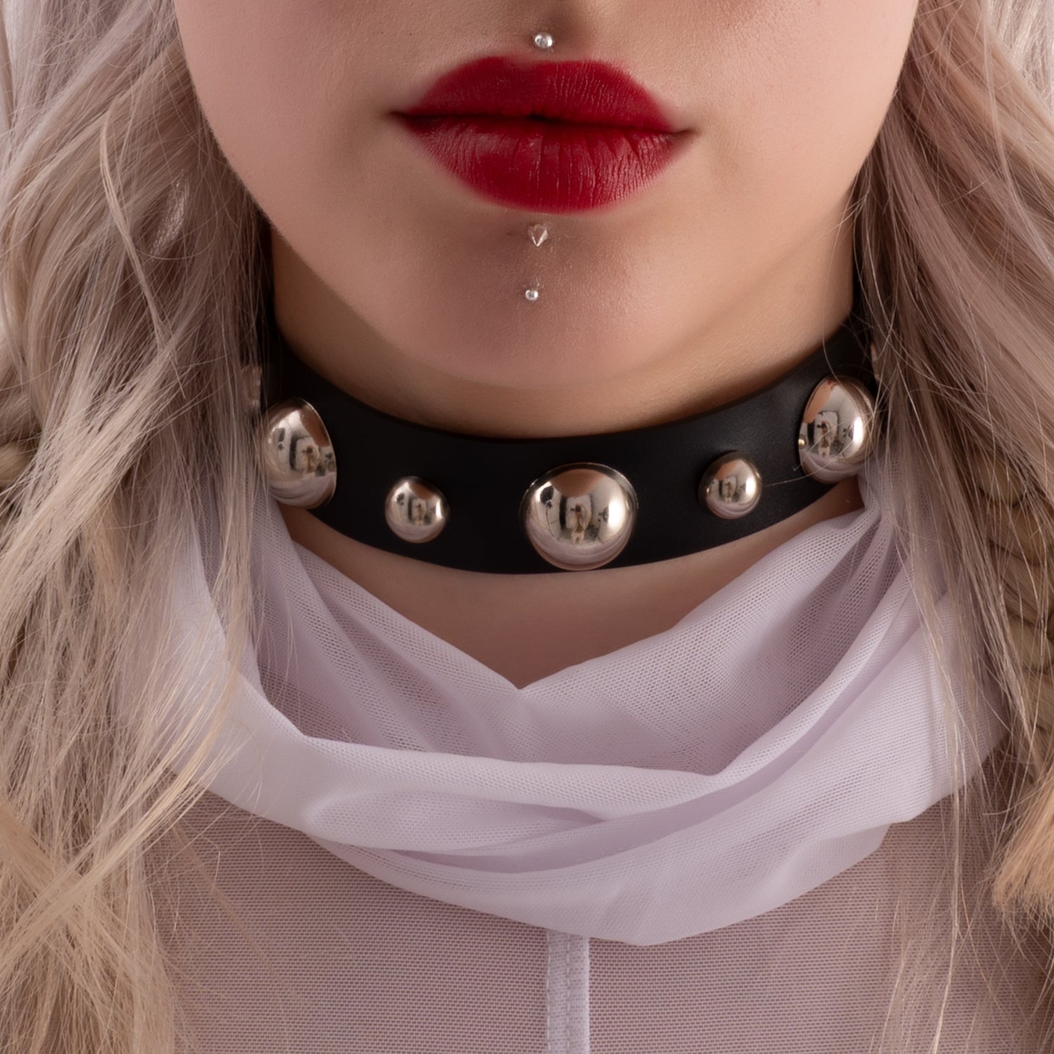 The image features a close-up of a woman wearing a bold black choker with large metallic spheres and a white sheer fabric draped around her shoulders. The overall look is edgy and statement-making, perfect for alternative fashion styles.