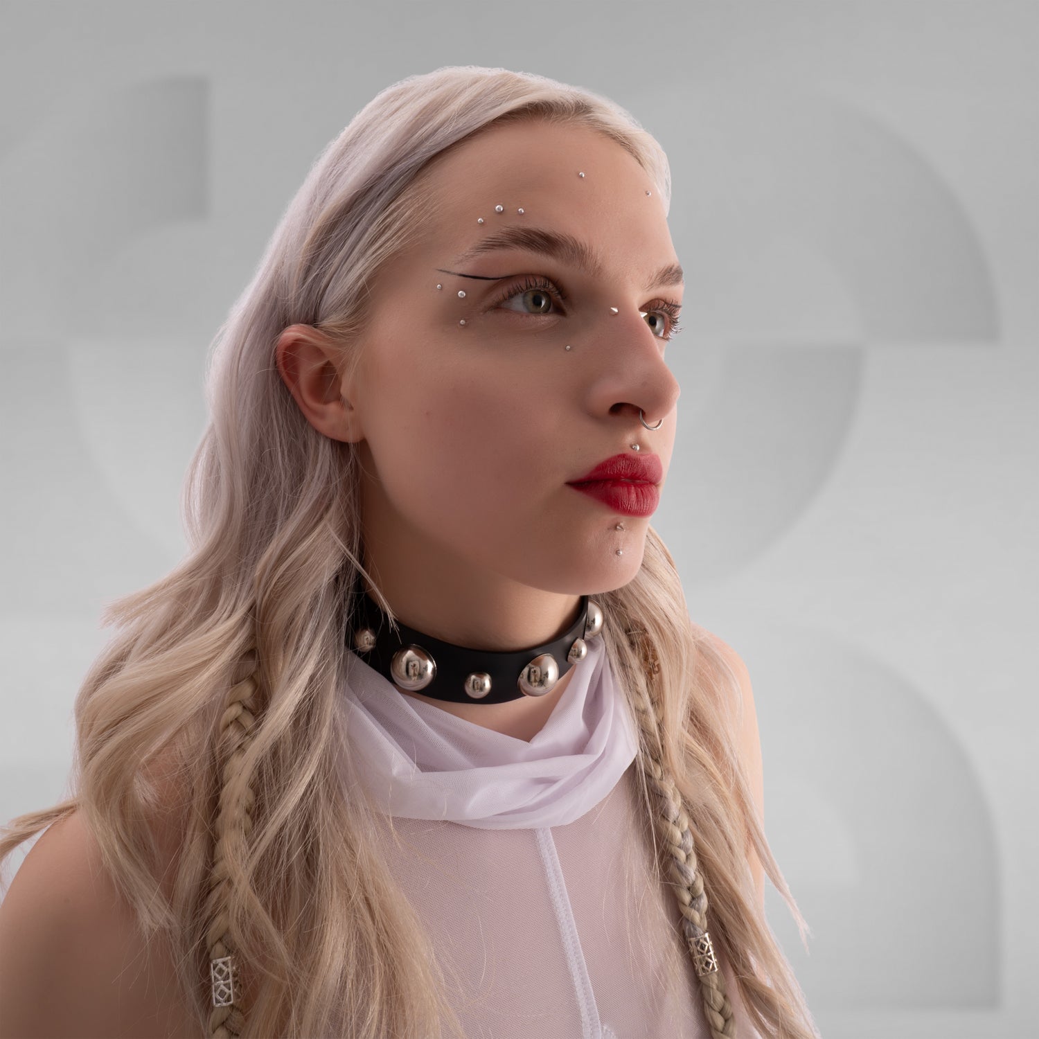 The image features a close-up of a woman wearing a bold black choker with large metallic spheres and a white sheer fabric draped around her shoulders. The overall look is edgy and statement-making, perfect for alternative fashion styles.