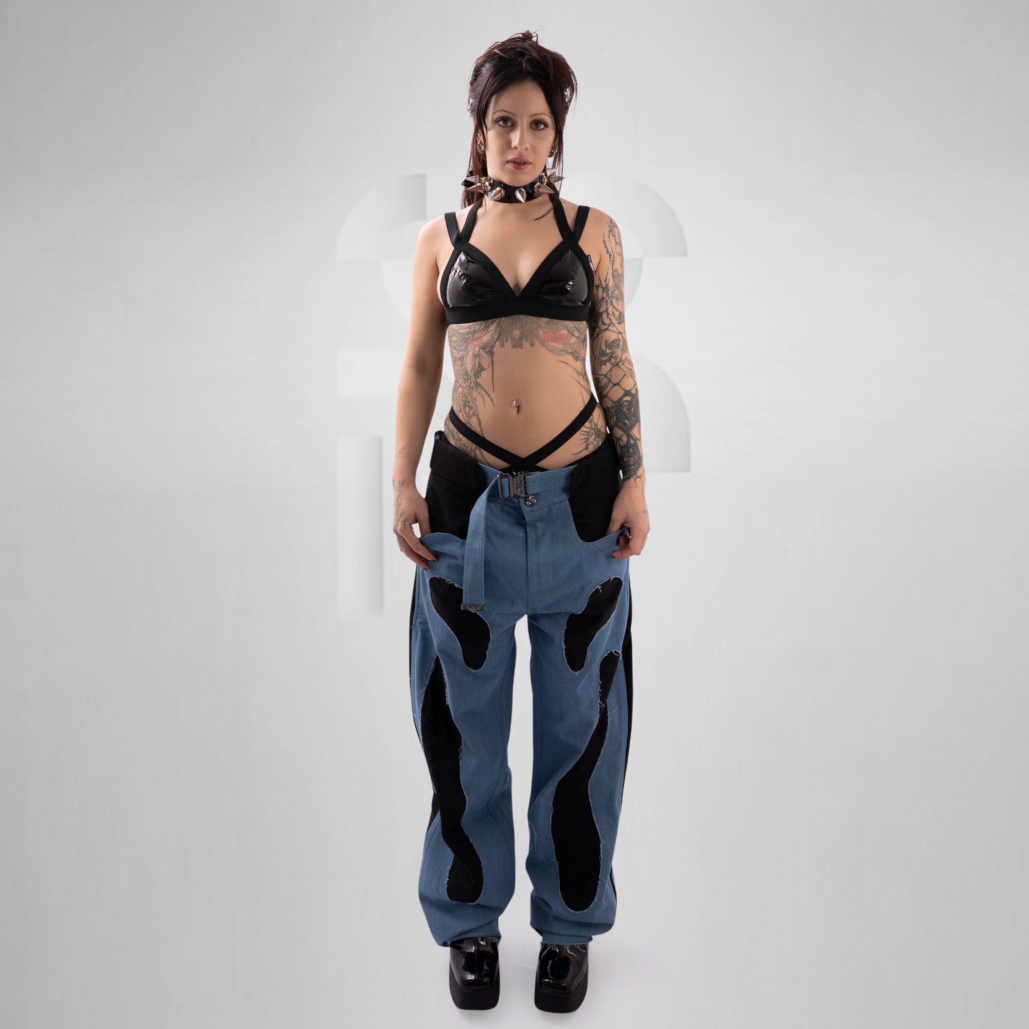 Person wearing a black lace top and blue jeans with black patches on a white background