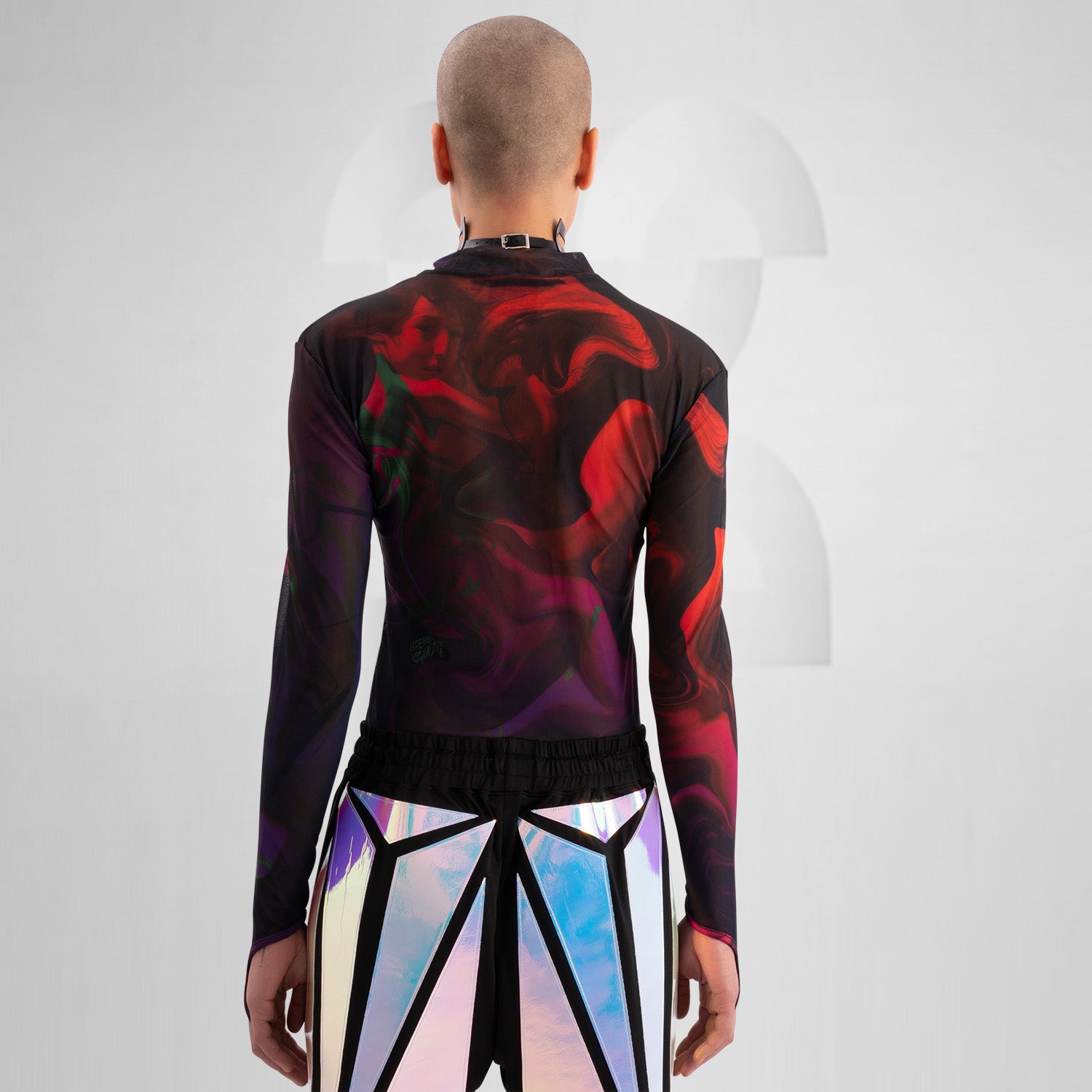 The image features a striking outfit showcasing a long-sleeve top with a captivating abstract design in rich hues of red and purple. Its unique metallic neck detail adds an edgy touch, perfectly complementing the bold, artistic style. The top is paired with eye-catching shorts featuring reflective panels, creating a dynamic look that's perfect for standing out. This ensemble is ideal for nightlife events or fashion-forward gatherings, exuding confidence and individuality while embracing a modern aesthetic.