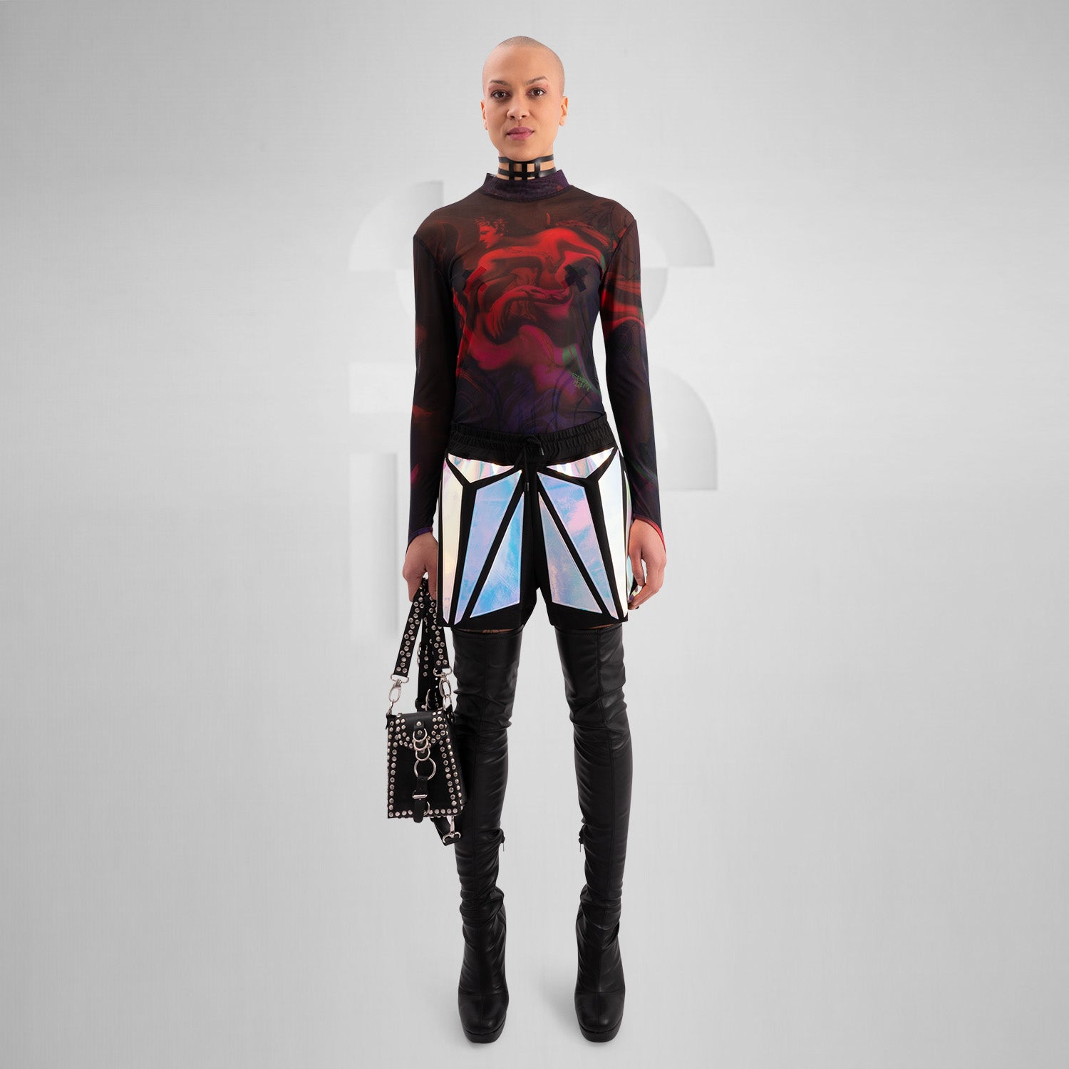 The image features a striking outfit showcasing a long-sleeve top with a captivating abstract design in rich hues of red and purple. Its unique metallic neck detail adds an edgy touch, perfectly complementing the bold, artistic style. The top is paired with eye-catching shorts featuring reflective panels, creating a dynamic look that's perfect for standing out. This ensemble is ideal for nightlife events or fashion-forward gatherings, exuding confidence and individuality while embracing a modern aesthetic.
