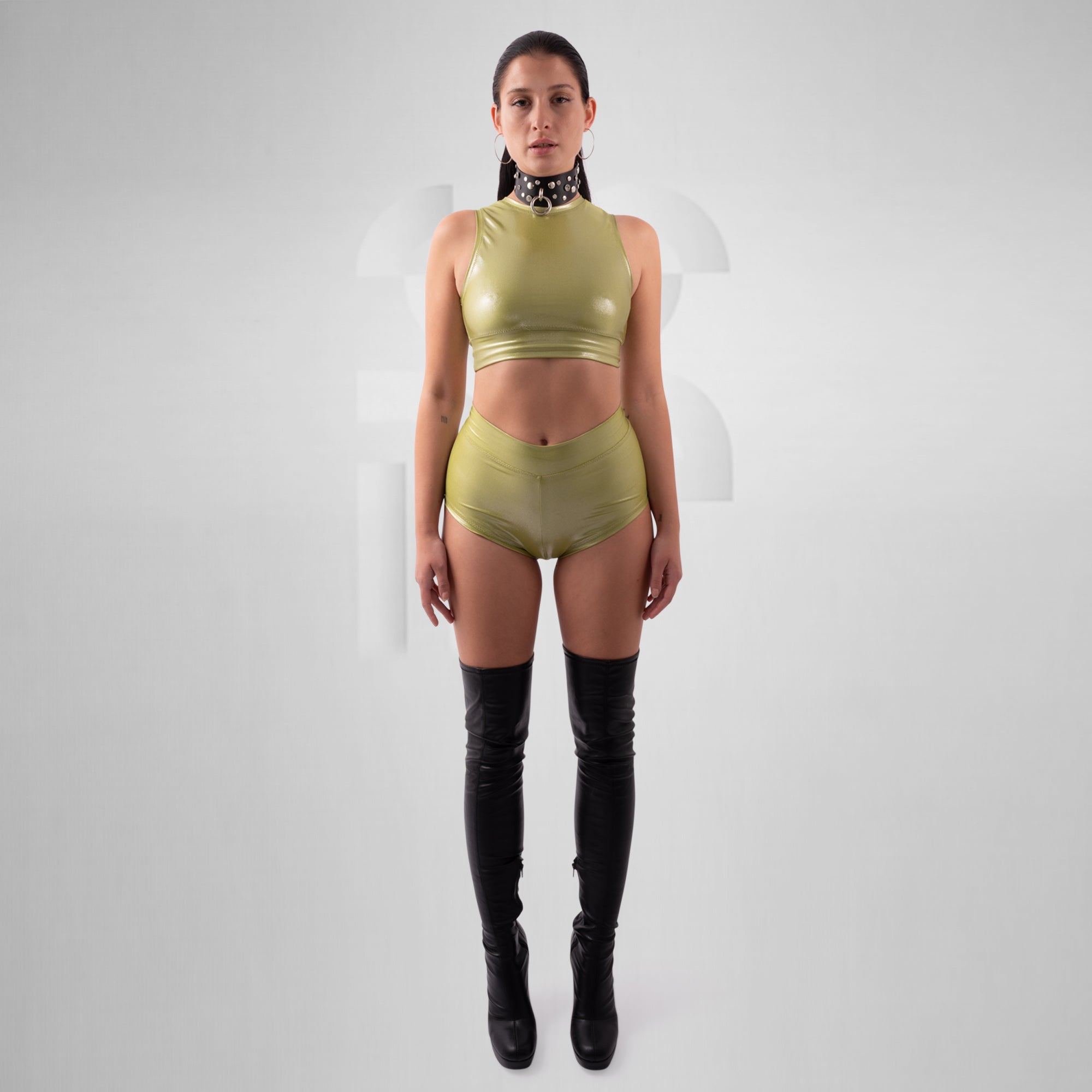 Person wearing a green sleeveless top and matching shorts with black knee-high boots on a white background