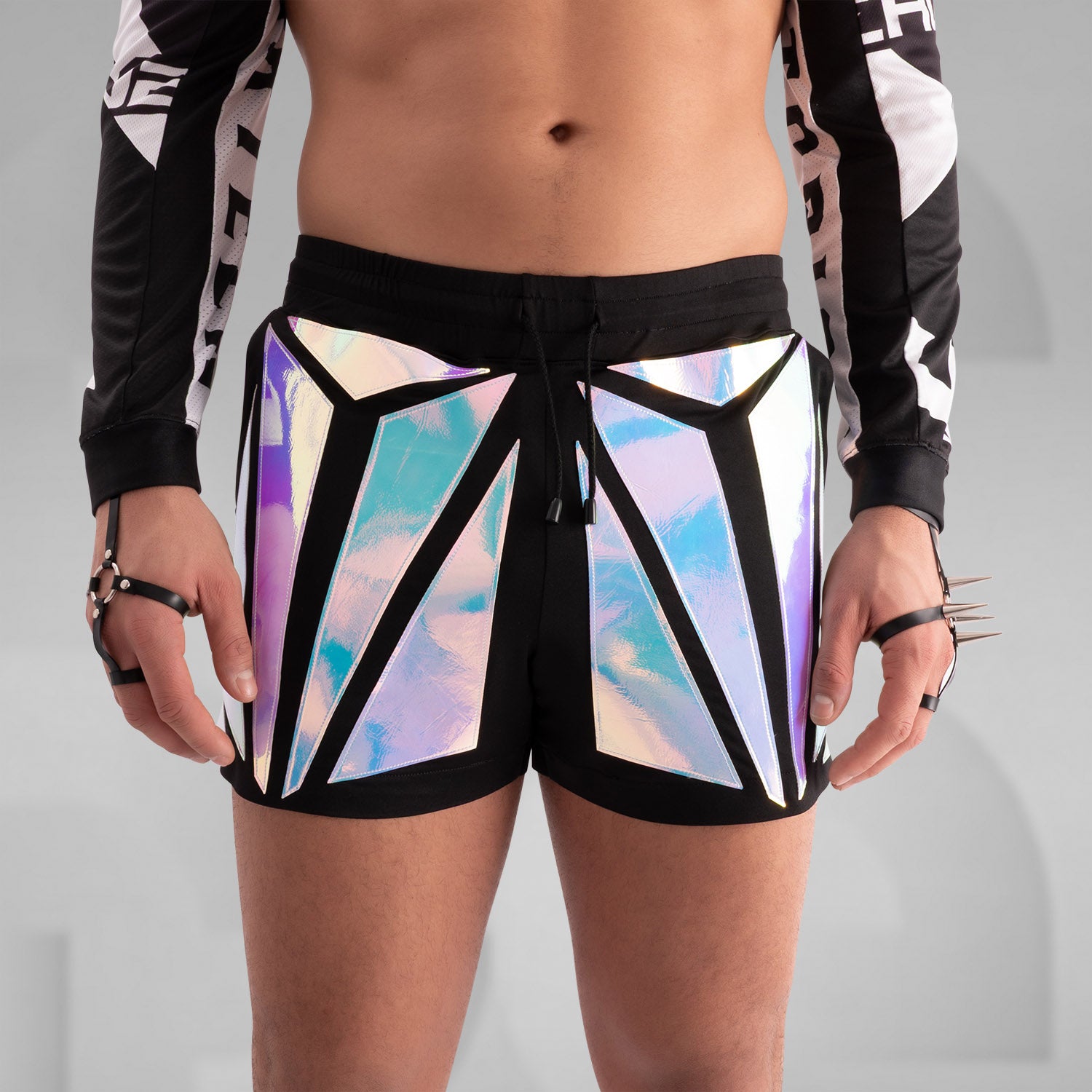 Close-up of a model wearing black shorts with striking holographic geometric panels, reflecting iridescent colors. Paired with a sheer long-sleeve top and thigh-high black leather boots, this futuristic and edgy look is perfect for festival, rave, and avant-garde fashion.