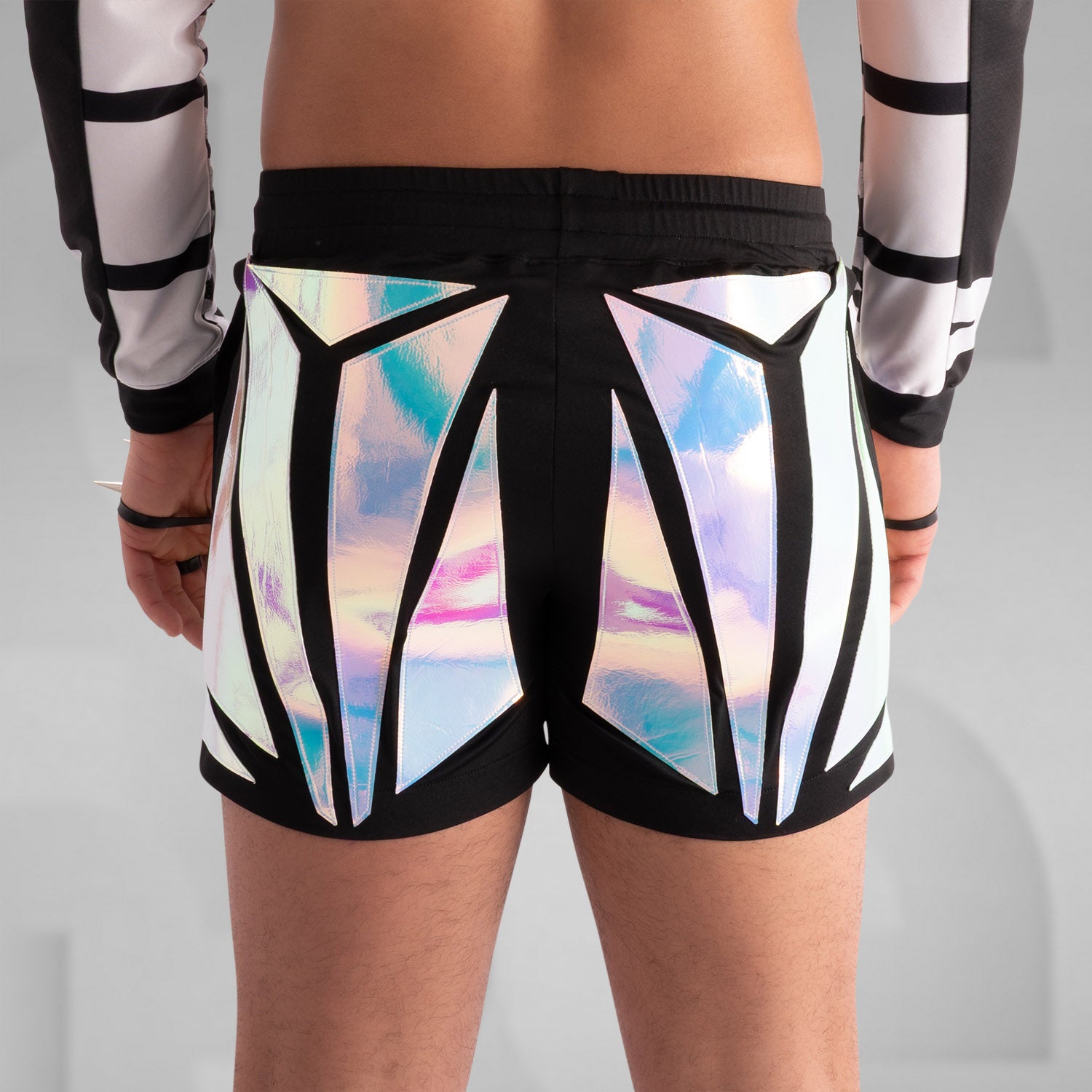 Close-up of a model wearing black shorts with striking holographic geometric panels, reflecting iridescent colors. Paired with a sheer long-sleeve top and thigh-high black leather boots, this futuristic and edgy look is perfect for festival, rave, and avant-garde fashion.