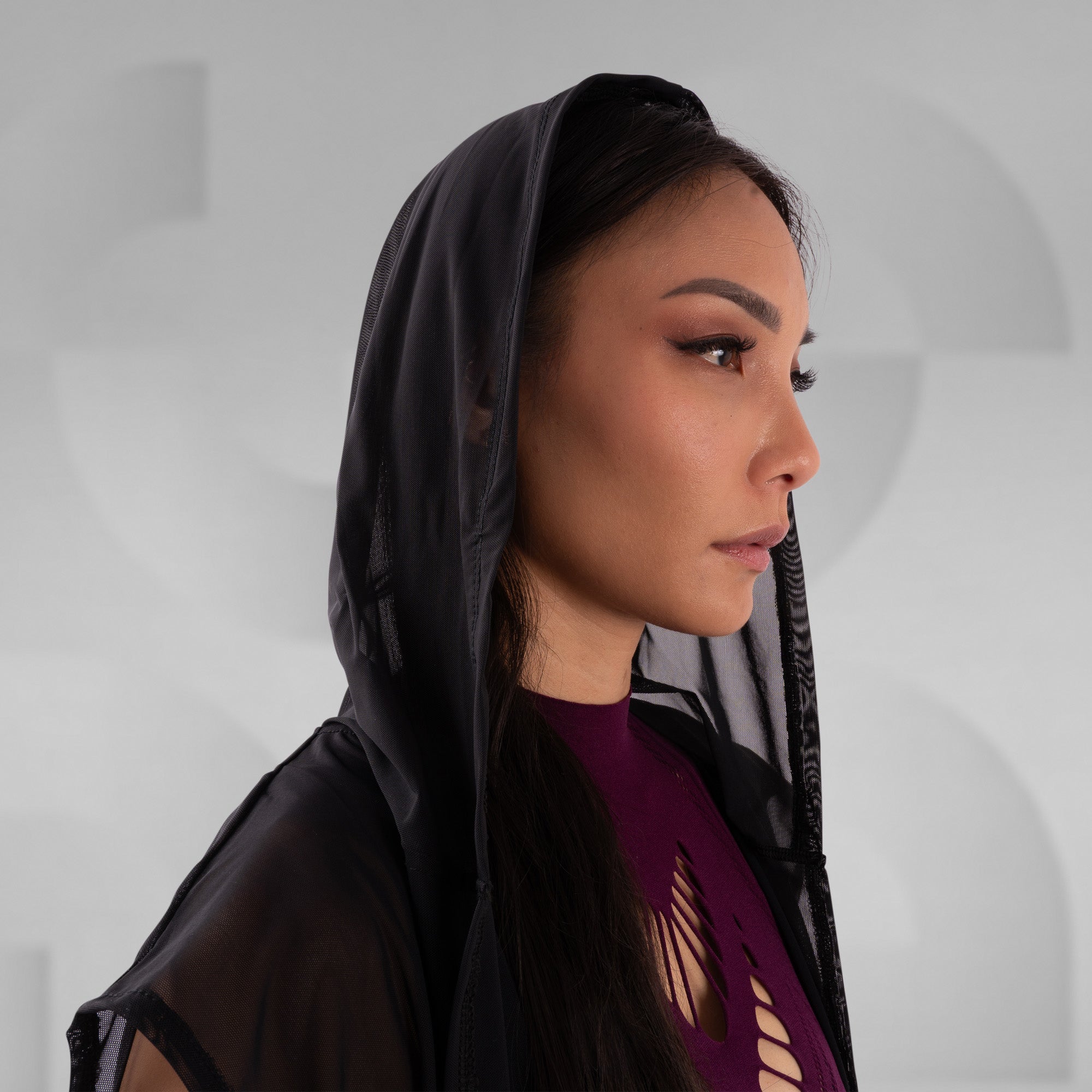 Woman wearing a black hooded garment against a neutral background