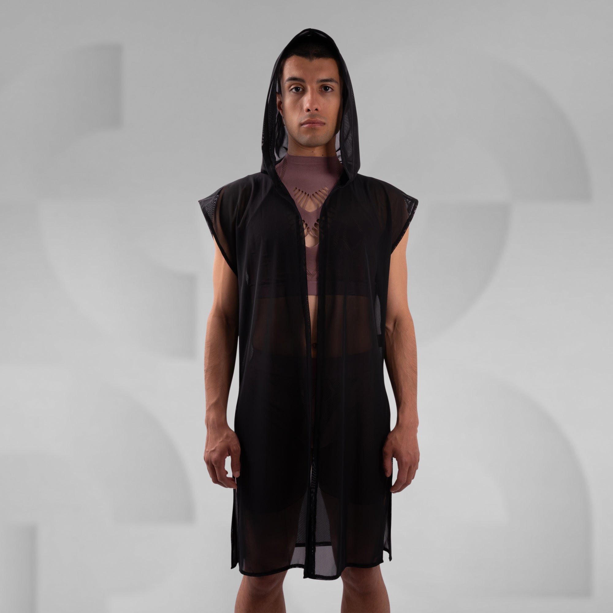 Person wearing a black sleeveless dress with a hood on a gray background