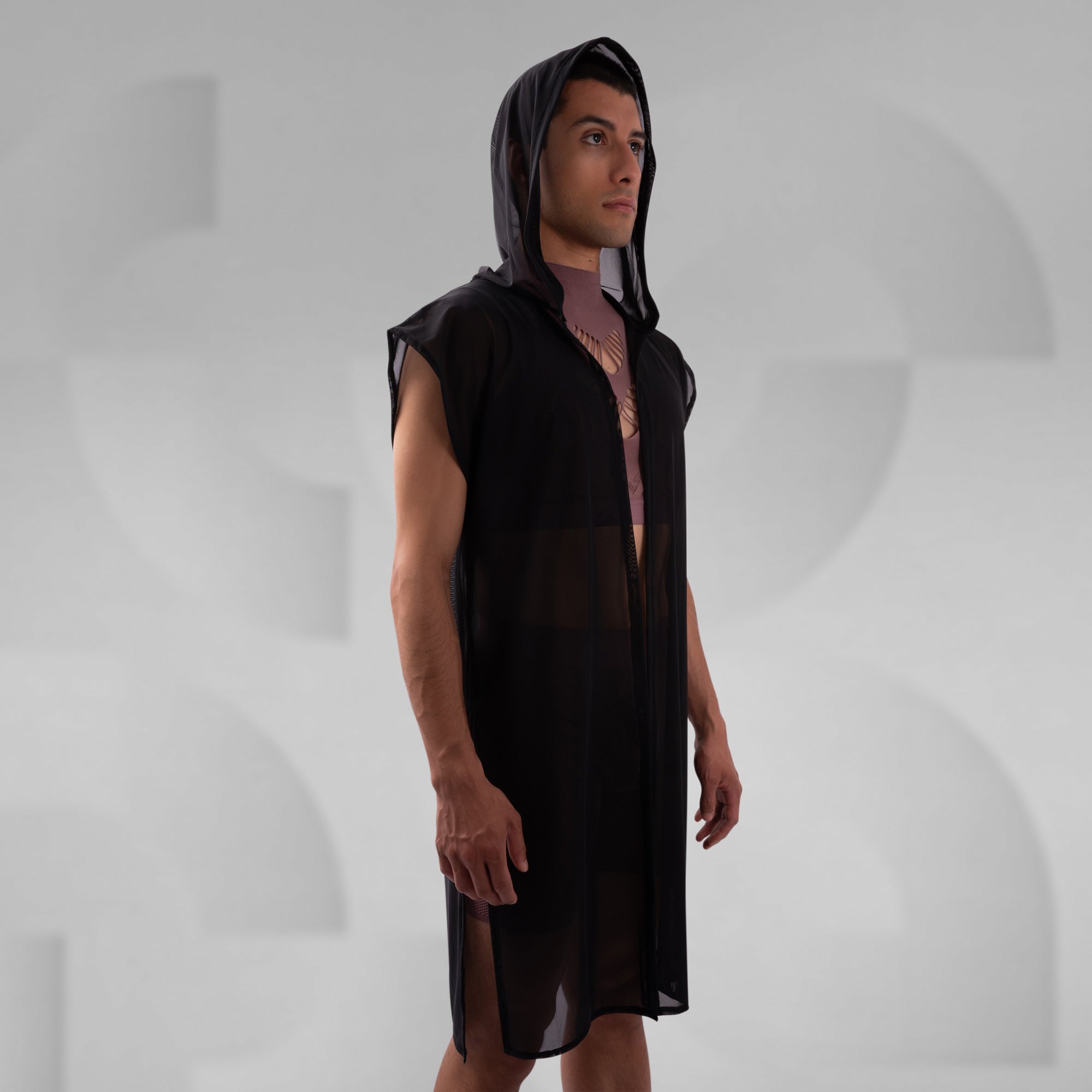 Person wearing a black sleeveless hooded garment on a gray background