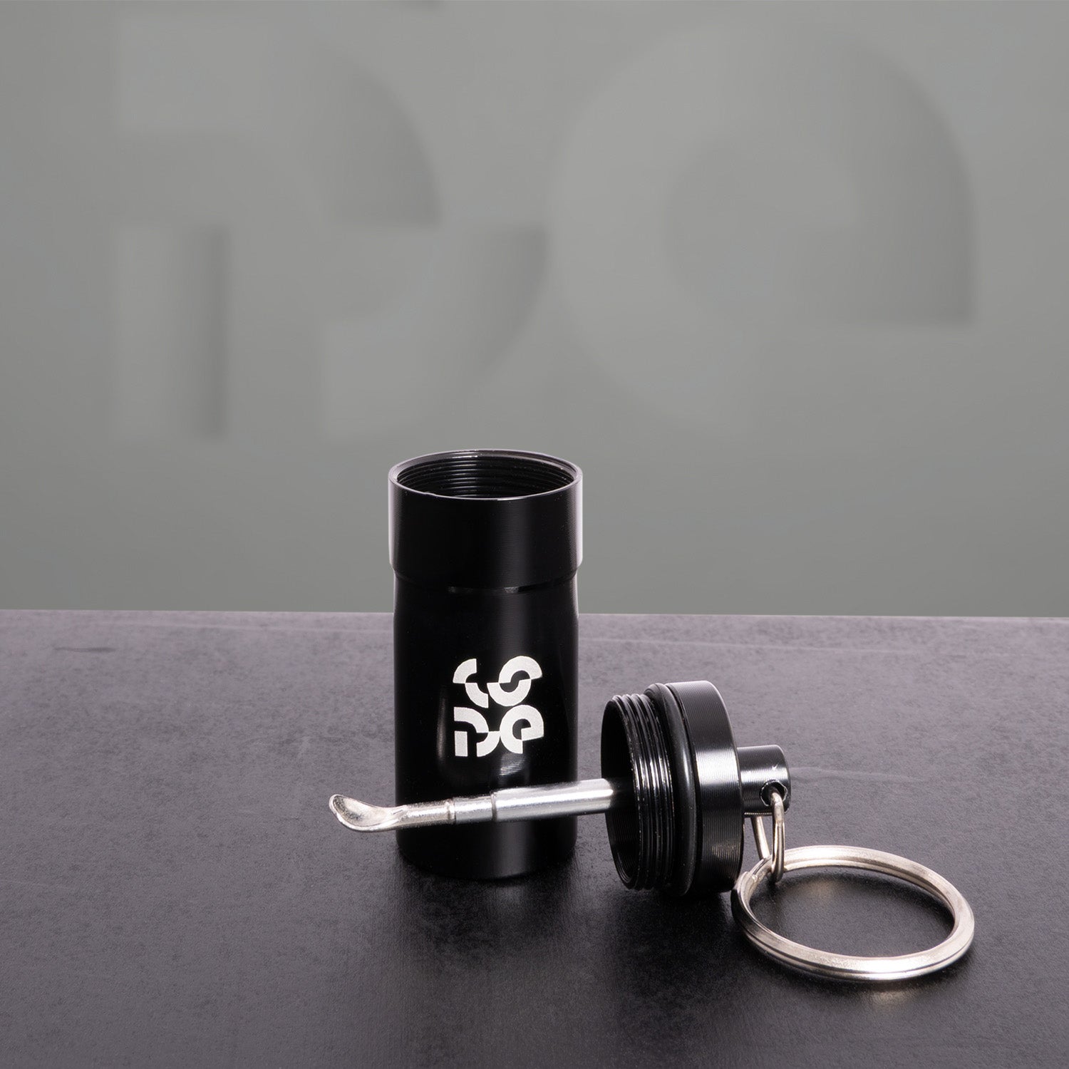 The image features a sleek black keychain accessory with a modern design. It includes a cylindrical container and a tool attached to a keyring, showcasing practicality and style. This type of accessory is ideal for those who appreciate functional items that complement their everyday carry. Perfect for storing small essentials or as a unique gift, it adds an edgy touch to any keychain collection.
