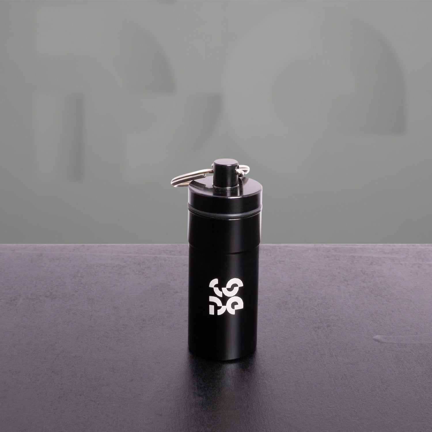The image features a sleek black keychain accessory with a modern design. It includes a cylindrical container and a tool attached to a keyring, showcasing practicality and style. This type of accessory is ideal for those who appreciate functional items that complement their everyday carry. Perfect for storing small essentials or as a unique gift, it adds an edgy touch to any keychain collection.