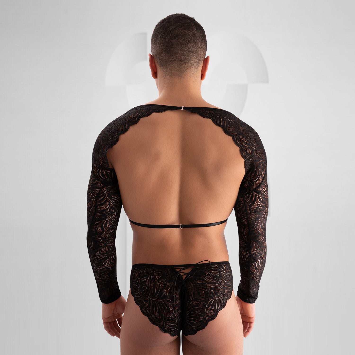 The outfit in the image consists of a bold, fashion-forward design. It features a black lace top with long sleeves and intricate patterns. The top is open at the chest with a strap across the front. The bottom is a matching black lace piece. This ensemble presents a unique and striking look, likely designed for an expressive or avant-garde fashion setting.
