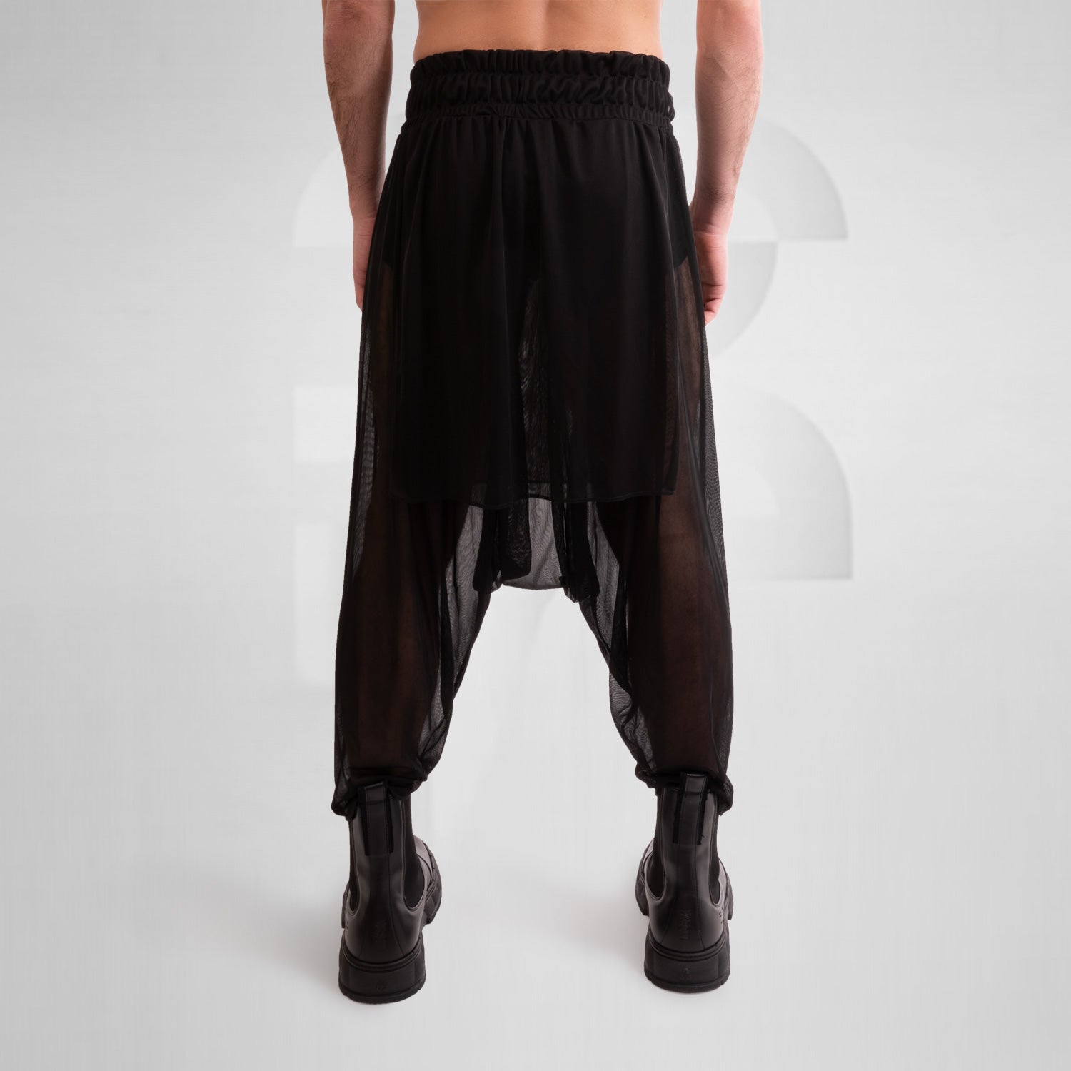 The Avantgarde Mesh Shorts from This is Fred feature a striking design with a unique silhouette and breathable mesh, ideal for festival and techno party vibes. The model showcases the shorts styled with bold black boots, emphasizing their edgy and fashionable appeal. Perfect for those looking to make a statement in their wardrobe.