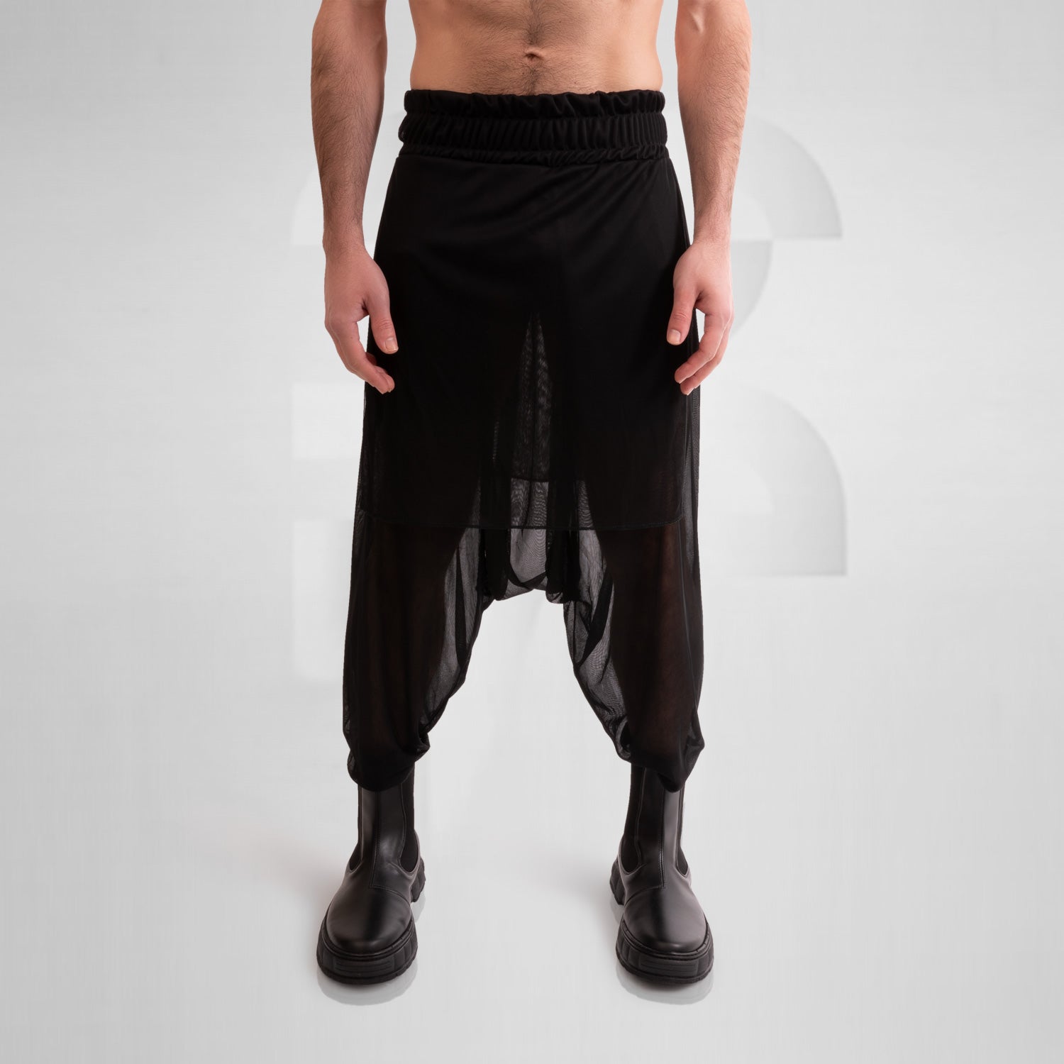 The Avantgarde Mesh Shorts from This is Fred feature a striking design with a unique silhouette and breathable mesh, ideal for festival and techno party vibes. The model showcases the shorts styled with bold black boots, emphasizing their edgy and fashionable appeal. Perfect for those looking to make a statement in their wardrobe.