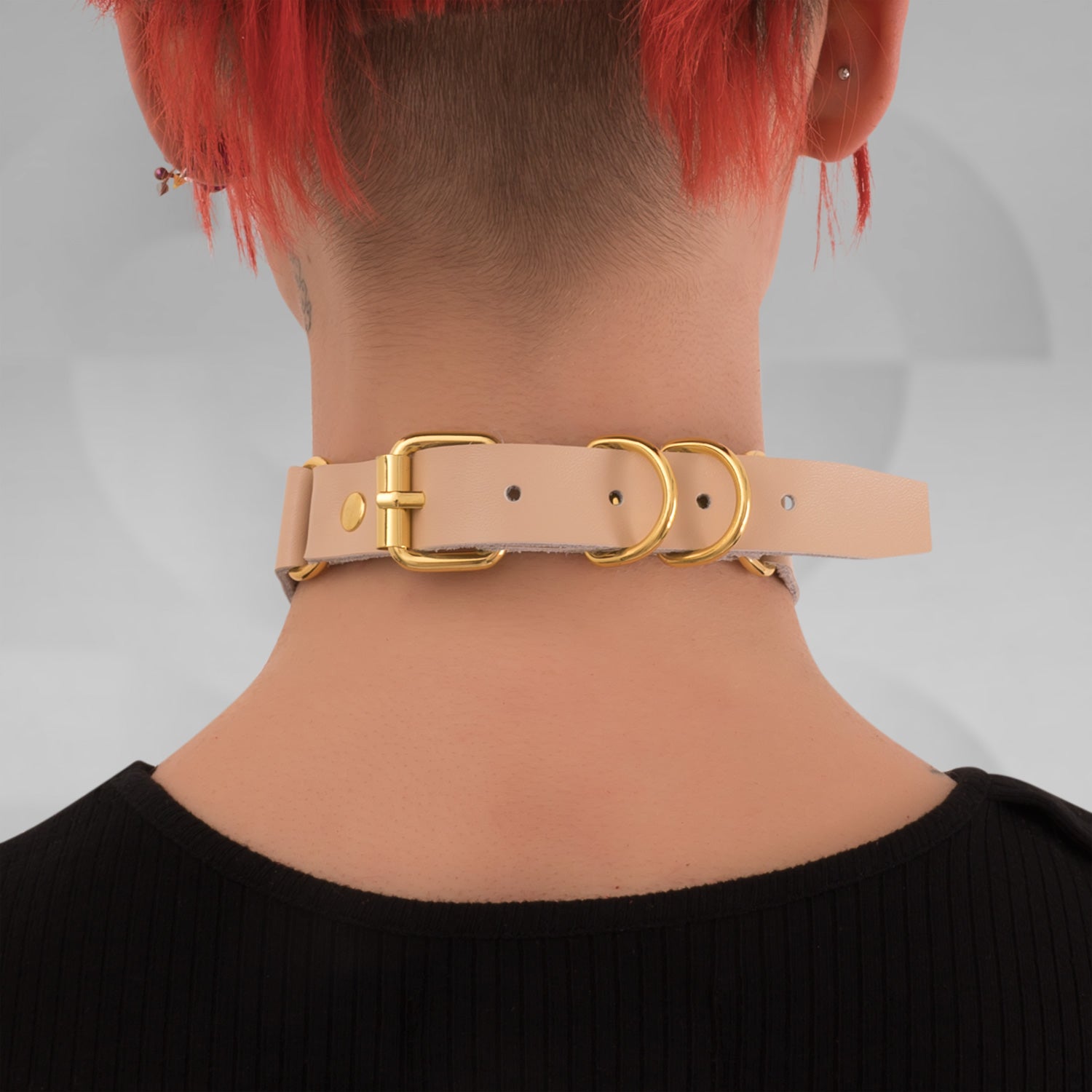 This image features a model wearing a chic nude leather choker that highlights its sophisticated design. The choker is adorned with prominent gold rings, creating a striking focal point that beautifully accentuates the neckline. Its elegant hue complements various styles, making it a versatile accessory for both casual outings and bold nightlife looks.