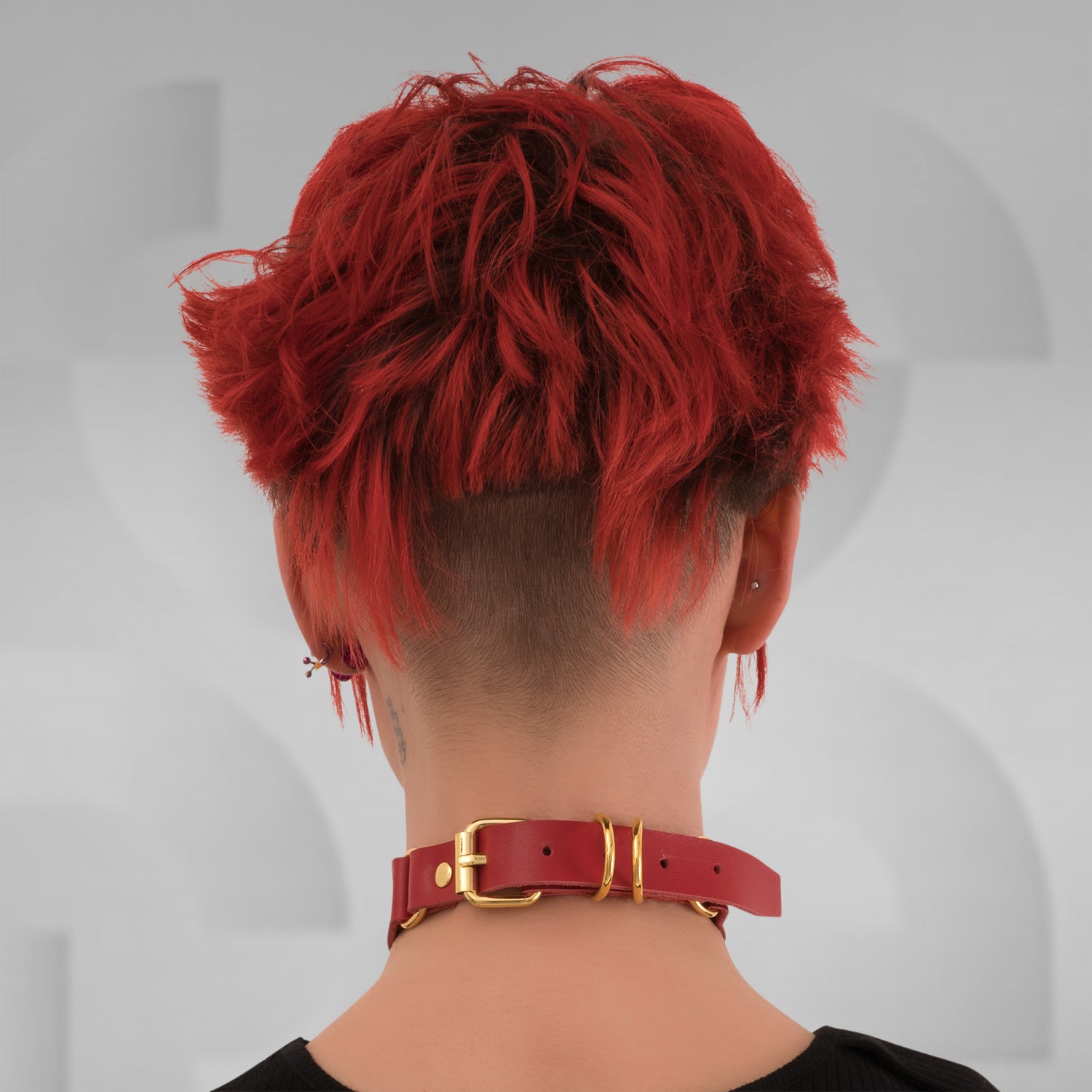 This image features a model wearing a striking red leather choker that showcases its bold design and contemporary flair. The choker features a prominent gold ring at the front, creating an eye-catching focal point that enhances the model's neckline and adds a touch of luxury to her look.