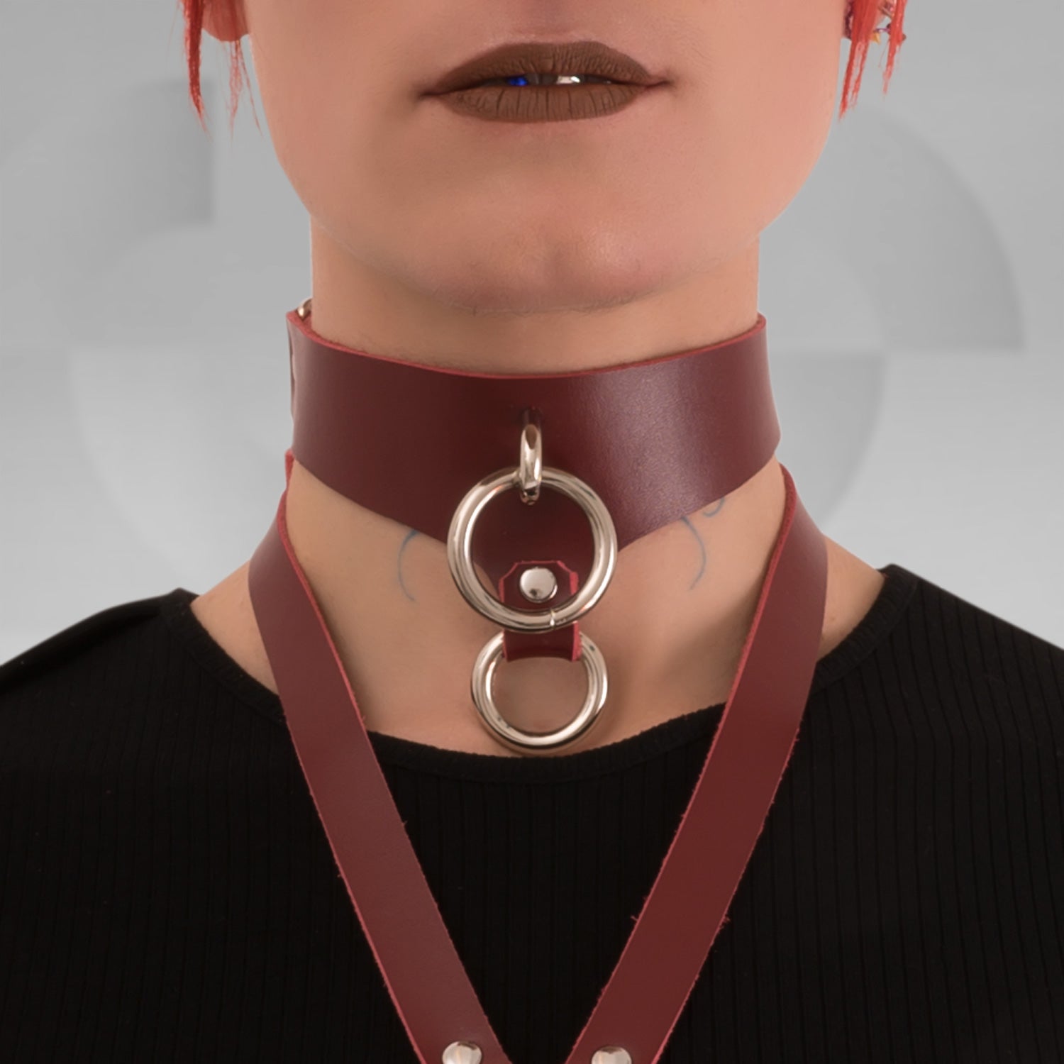 This image features a model wearing a bold red leather double ring choker, showcasing its striking design and luxurious quality. The choker is made from premium leather and features two silver rings at the front, creating a captivating focal point. Its rich burgundy hue beautifully complements the sleek lines of the choker, enhancing the model's neckline.