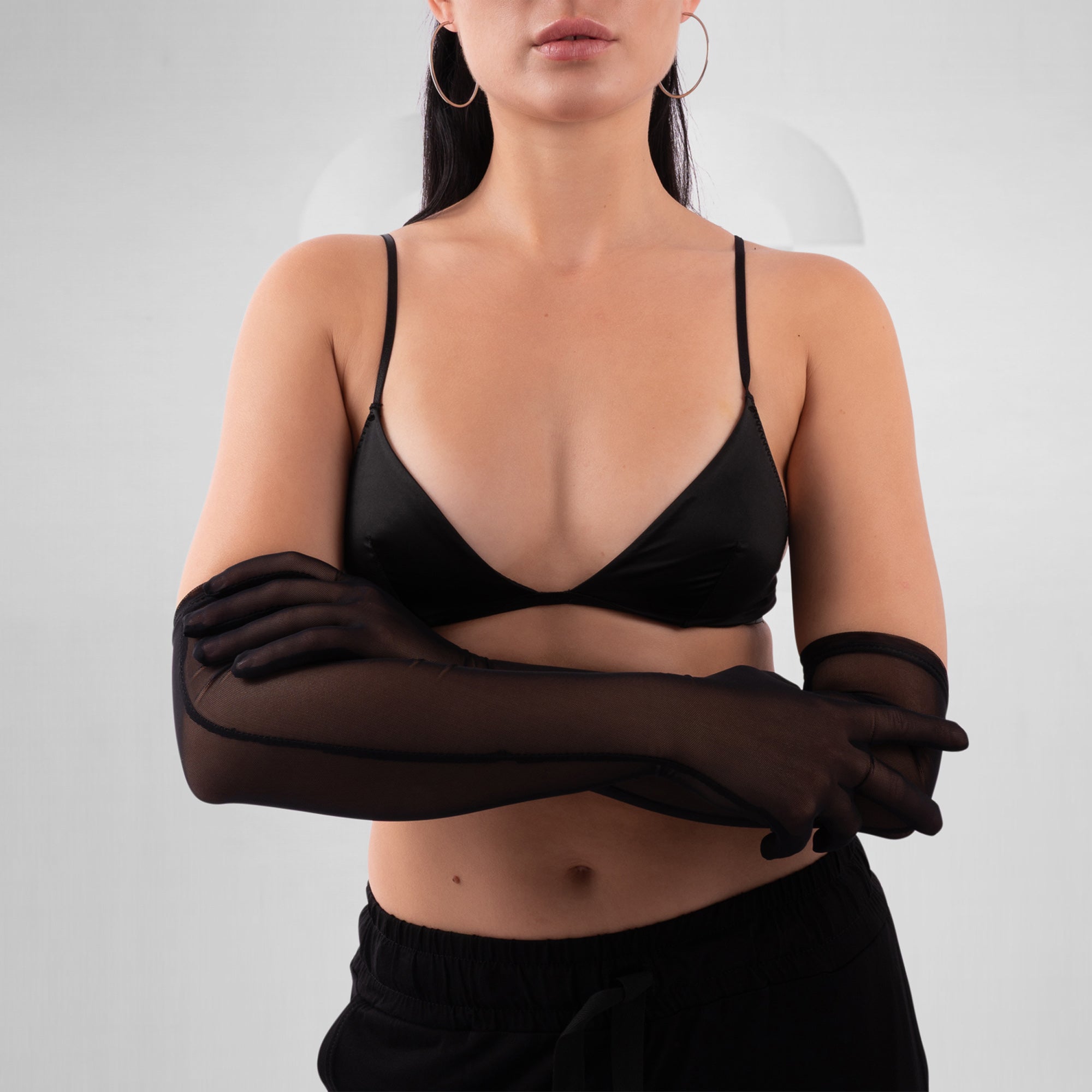 Person wearing a black bra and sheer black gloves on a plain background