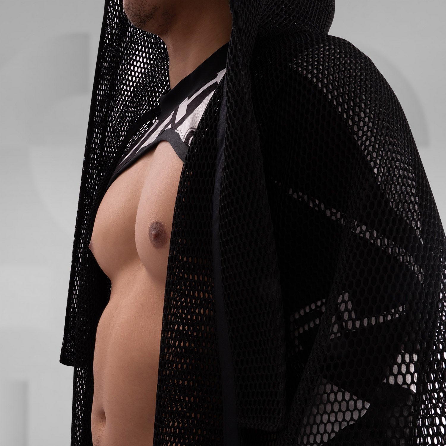 A model wearing a sheer black top with a dramatic black mesh floor-length robe, accessorized with a metallic collar, epitomizing avant-garde fashion and clubwear style, against a neutral gray background.
