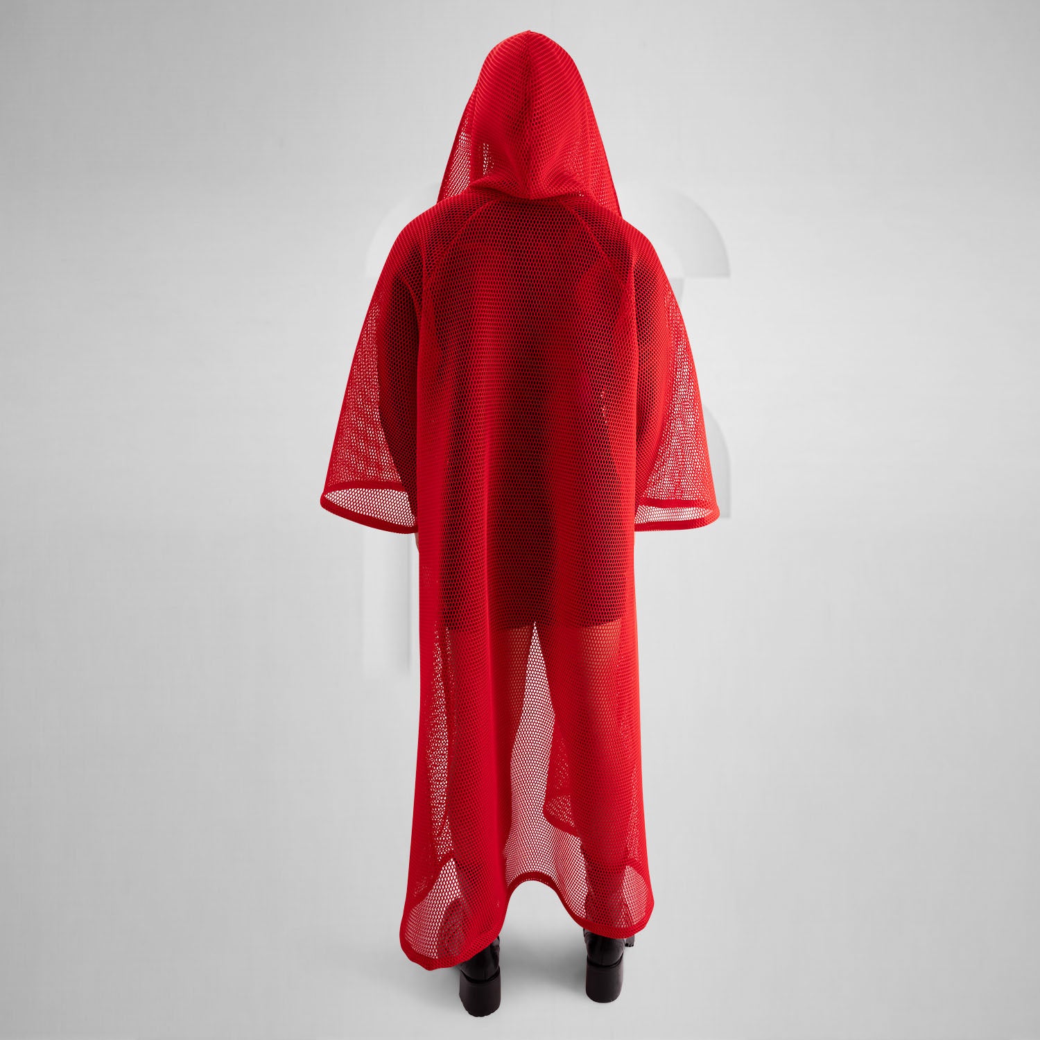 A model wearing a sheer black top with a dramatic red mesh floor-length robe, accessorized with a metallic collar, epitomizing avant-garde fashion and clubwear style, against a neutral gray background.