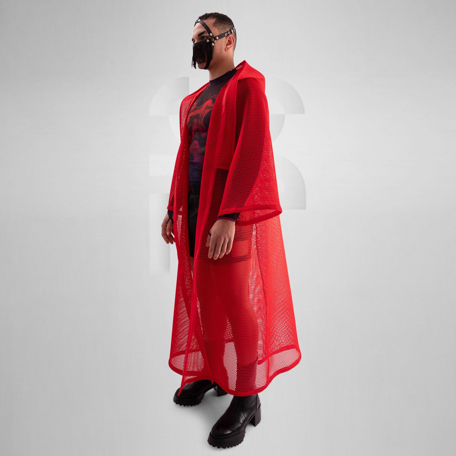 A model wearing a sheer black top with a dramatic red mesh floor-length robe, accessorized with a metallic collar, epitomizing avant-garde fashion and clubwear style, against a neutral gray background.