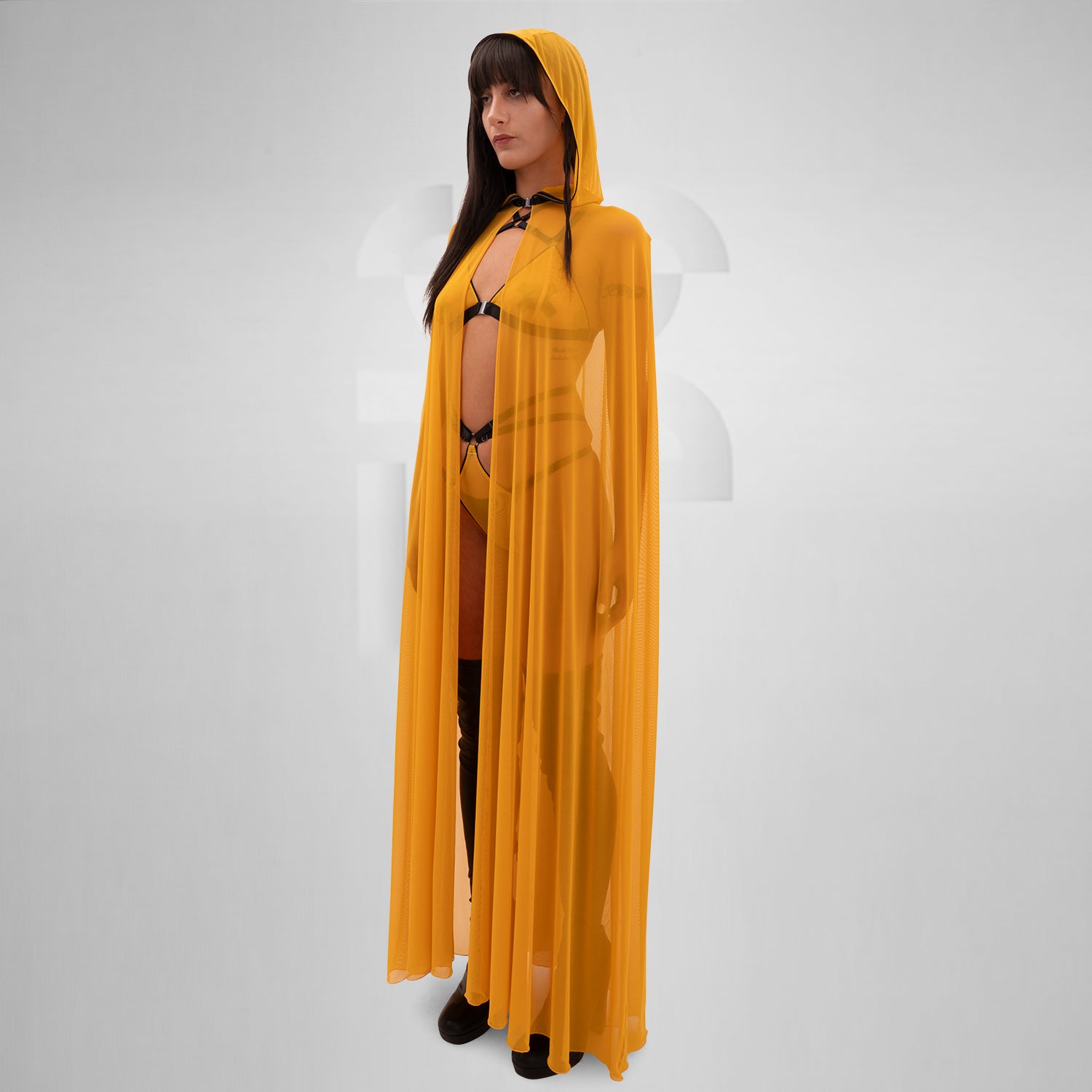 The image features a person wearing a flowing, sheer yellow cape that drapes elegantly to the floor. The cape is lightweight and creates a striking, dramatic silhouette. Underneath, the person is styled in minimal, edgy fashion, with strappy details adding a touch of avant-garde flair. The combination of the vibrant yellow cape and bold styling elements makes for a standout look that’s perfect for fashion-forward occasions.