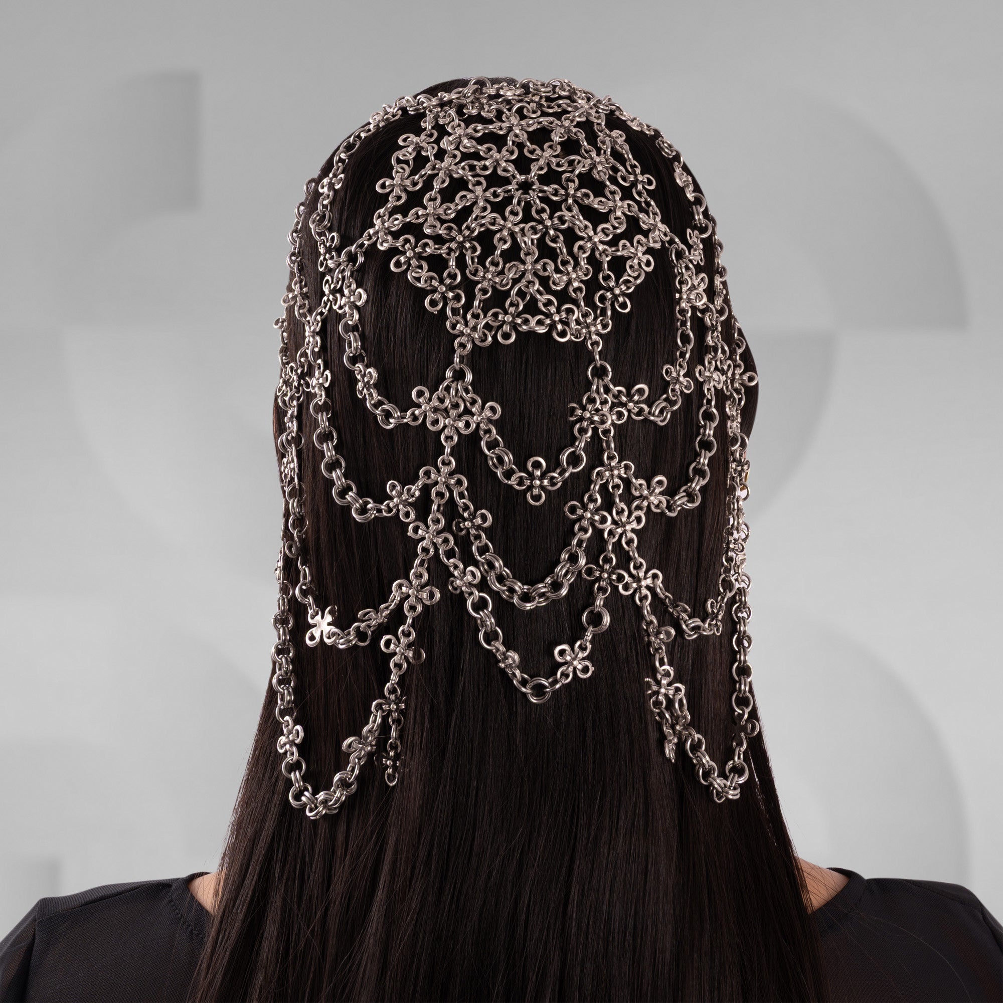 Person wearing a headpiece made of interlinked chains on a plain background